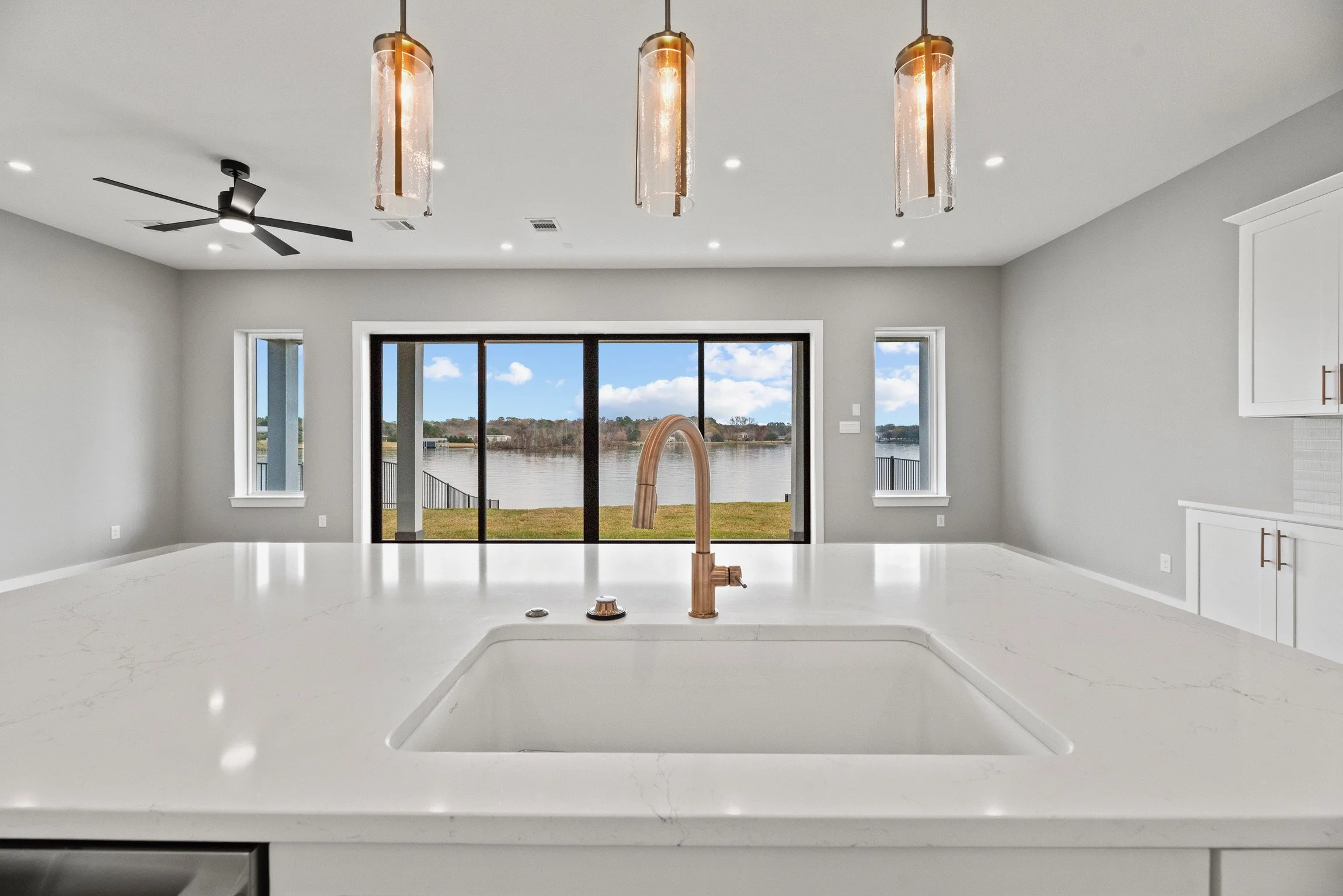 Modern kitchen with white countertops, rose gold faucet, large window with river view, and pendant lighting