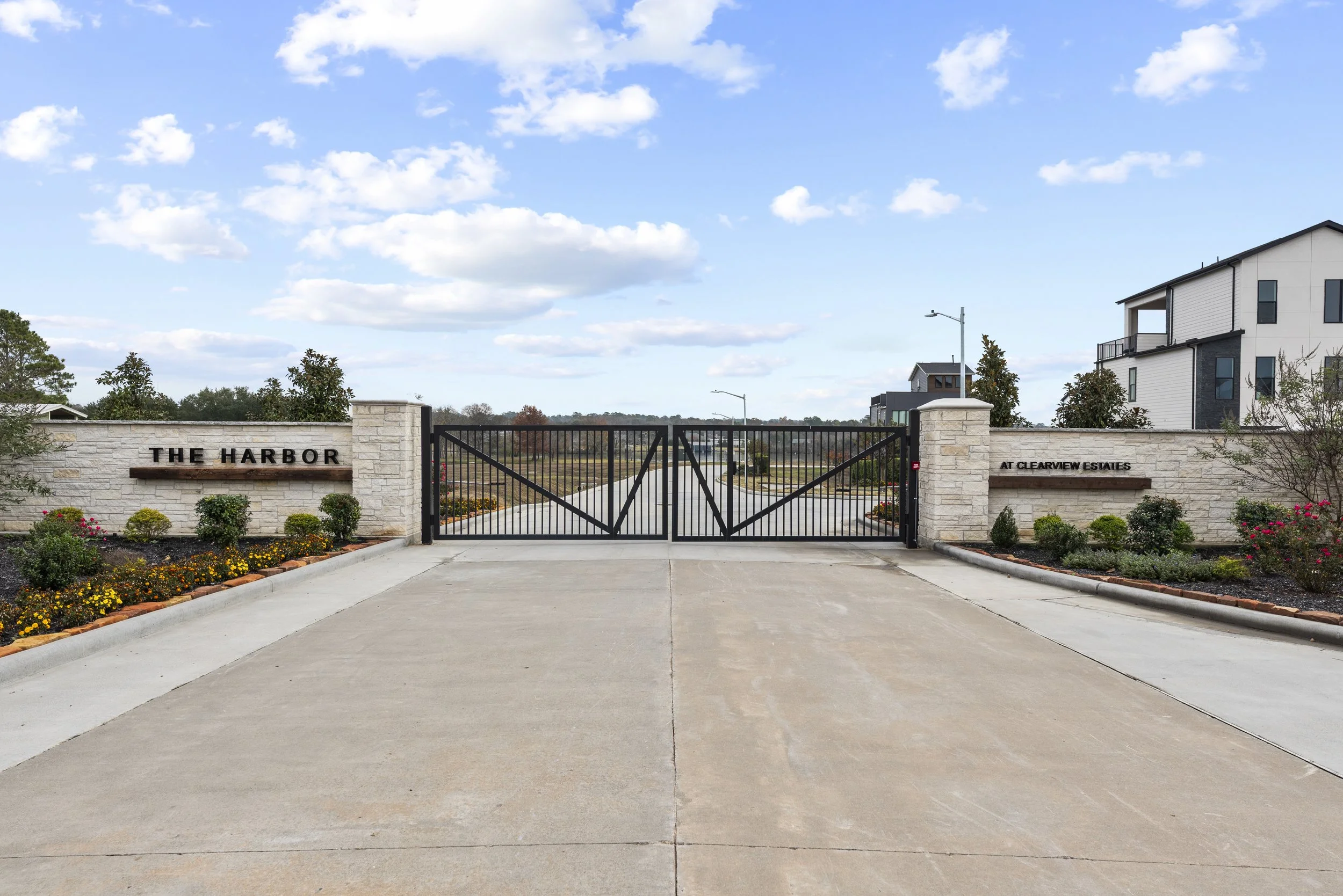 Aerial view of a waterfront residential neighborhood with houses along a calm water body, featuring a small green lawn, a curved walkway, and a white house on a narrow property.