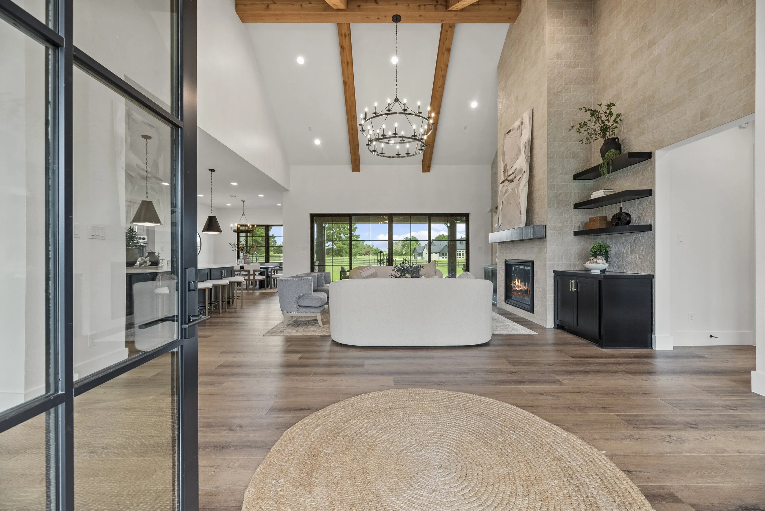 Spacious living room with high vaulted ceiling, wooden beams, modern fireplace, large window with scenic view, and contemporary furniture.