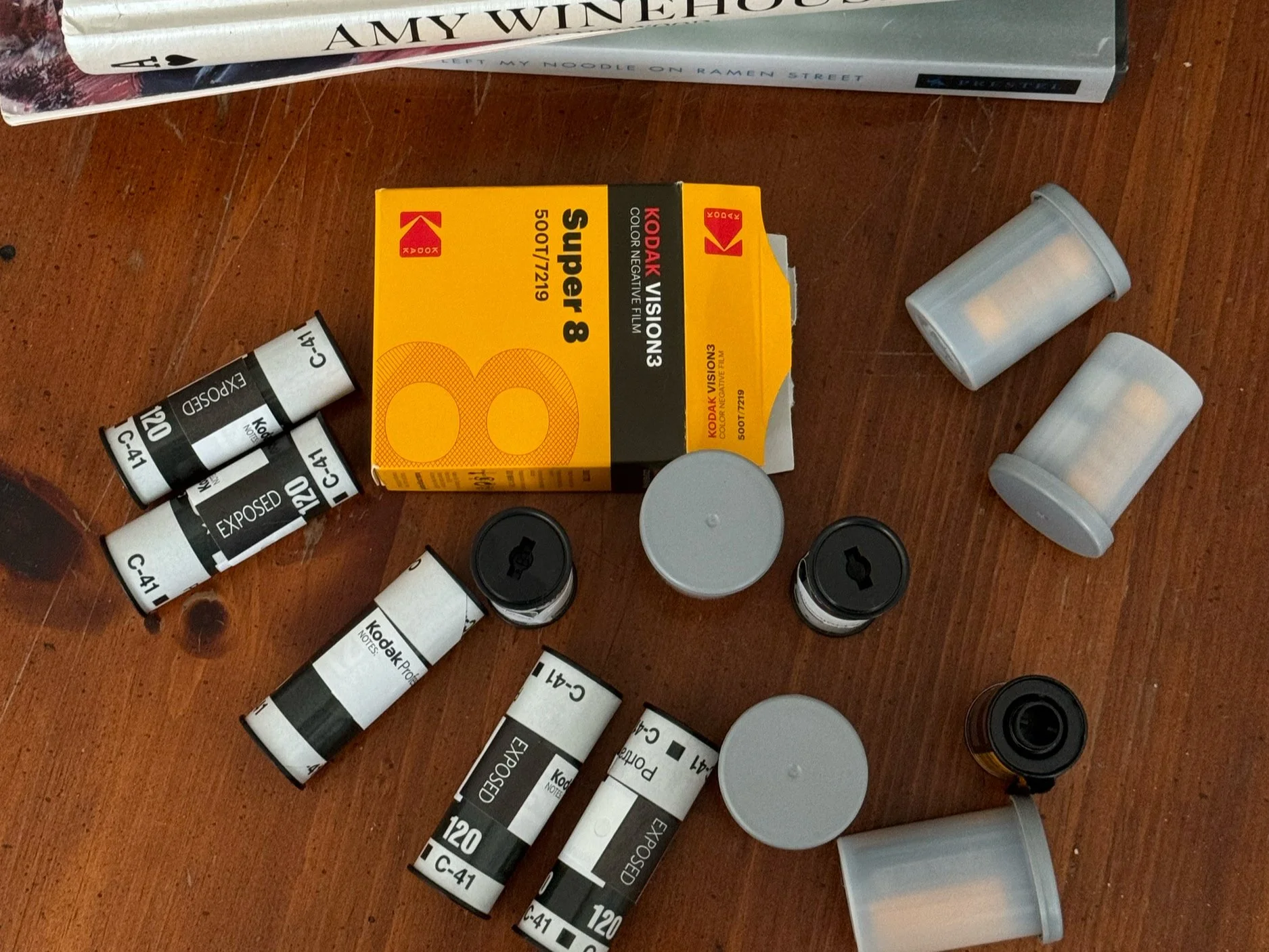 A collection of Kodak film rolls, film canisters, and a box of Kodak Vision3 Super 8 film on a wooden surface.