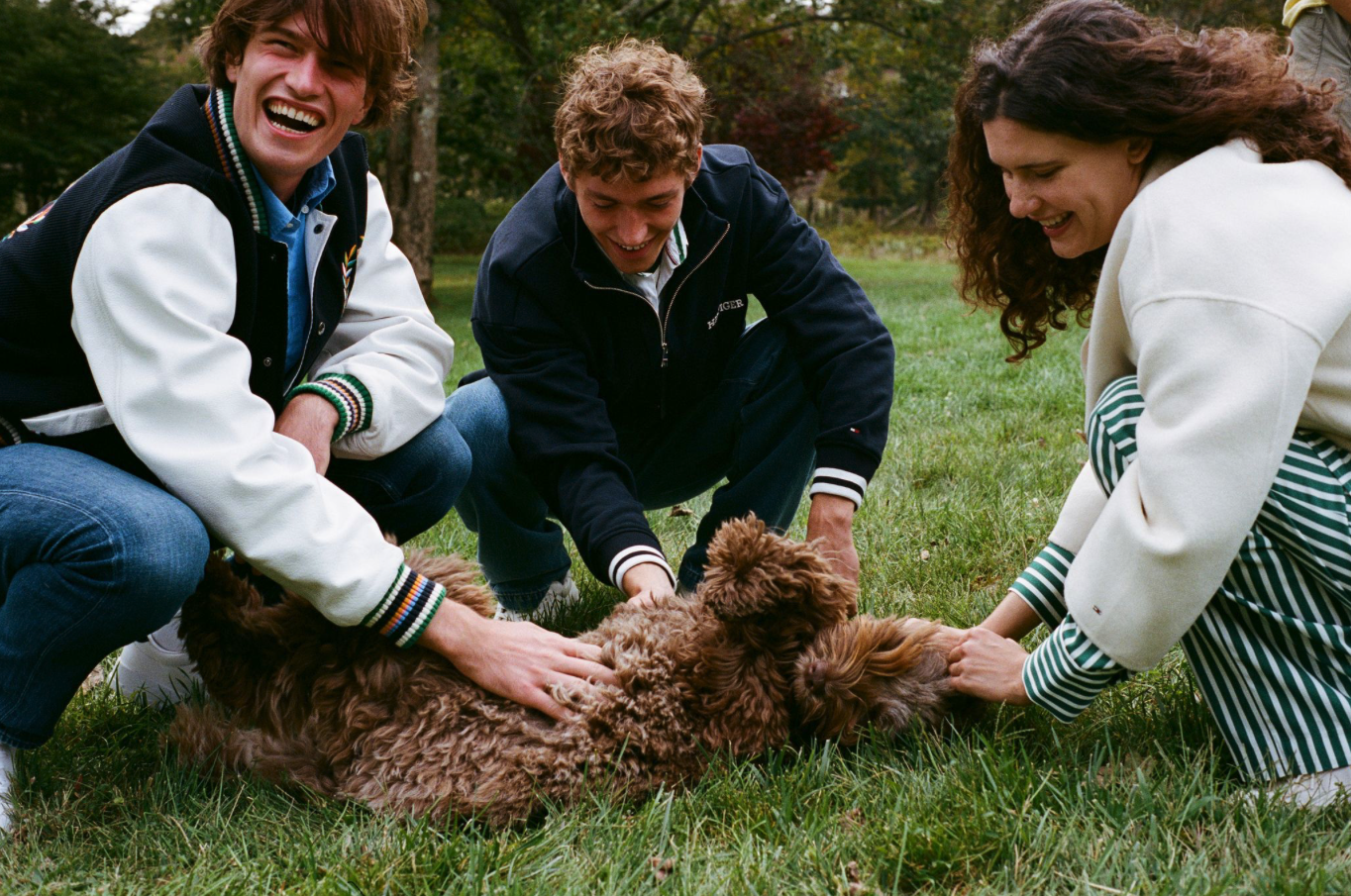 Three young adults playing with a curly brown dog on the grass outdoors, smiling and having fun.