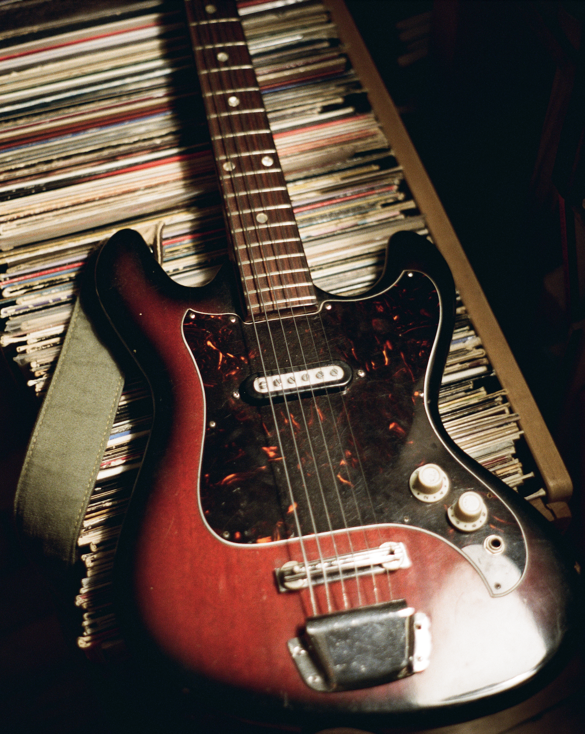 A vintage electric guitar with a sunburst finish resting on a surface covered with vinyl records.