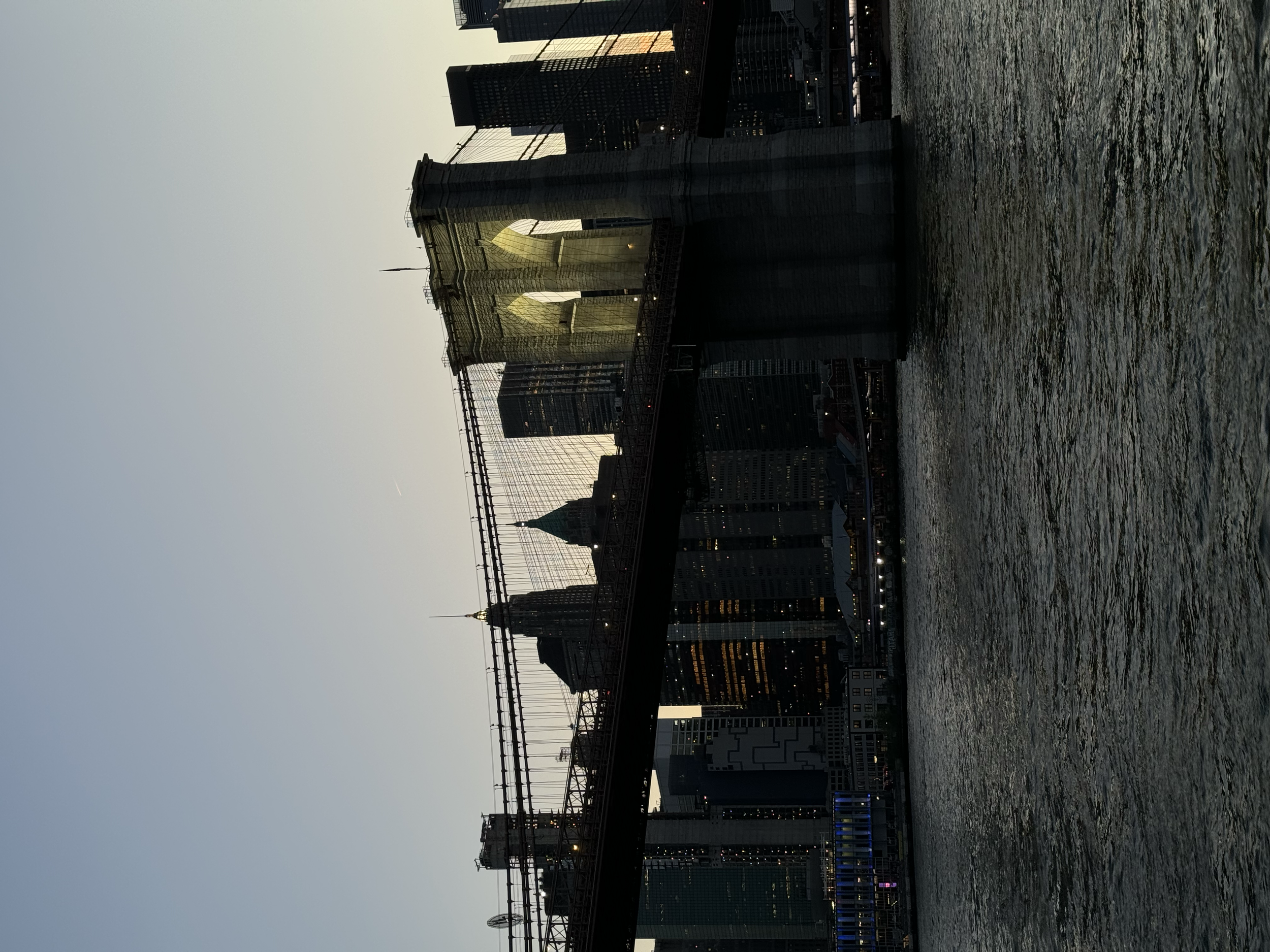View of Manhattan skyline and Brooklyn Bridge over water at dusk.