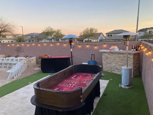 Outdoor area setup for event with craps table, bar, and string lights