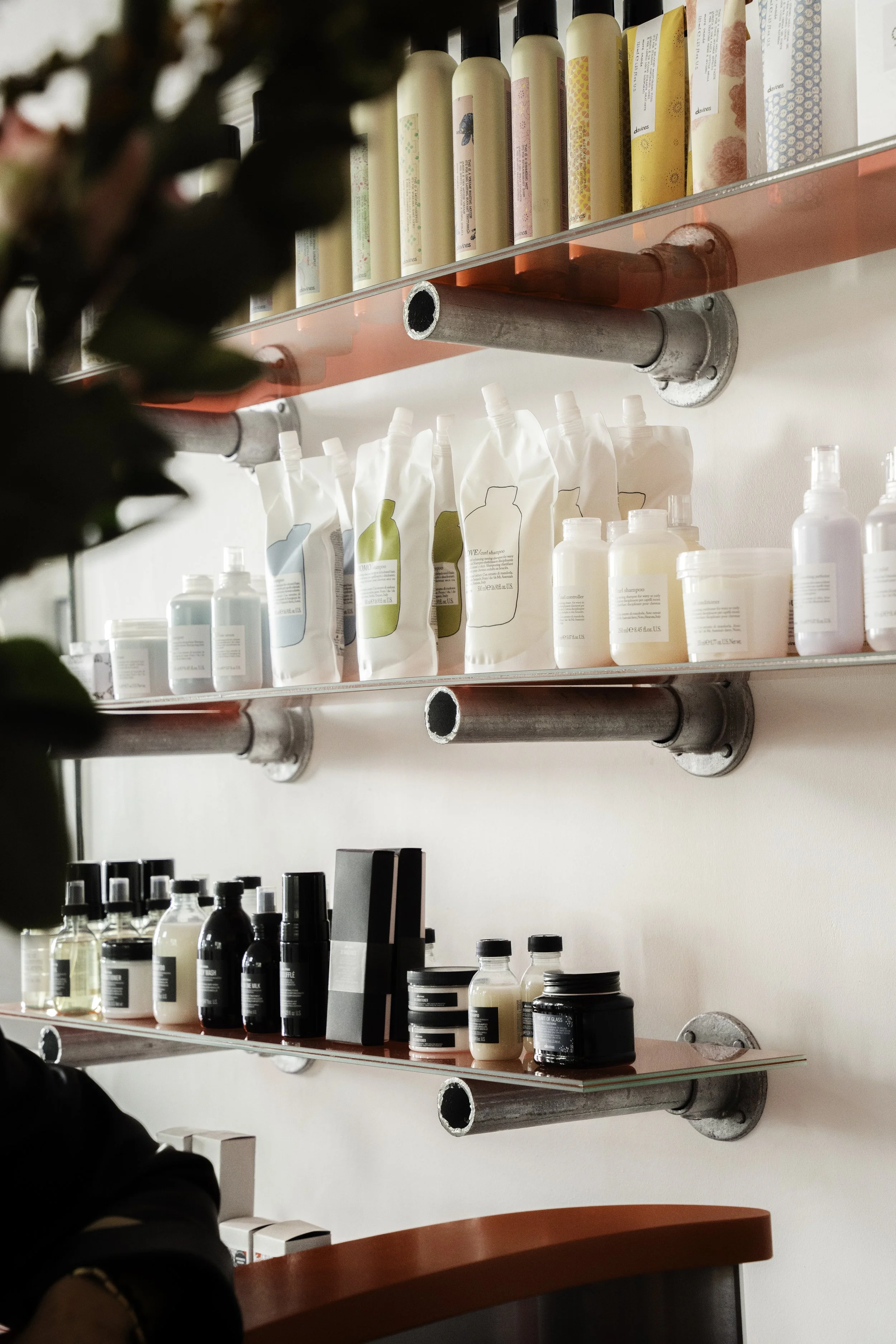 Hylder med forskellige plejeprodukter som flasker, krukker og pakker, monteret på en væg med metalrør i en butik.