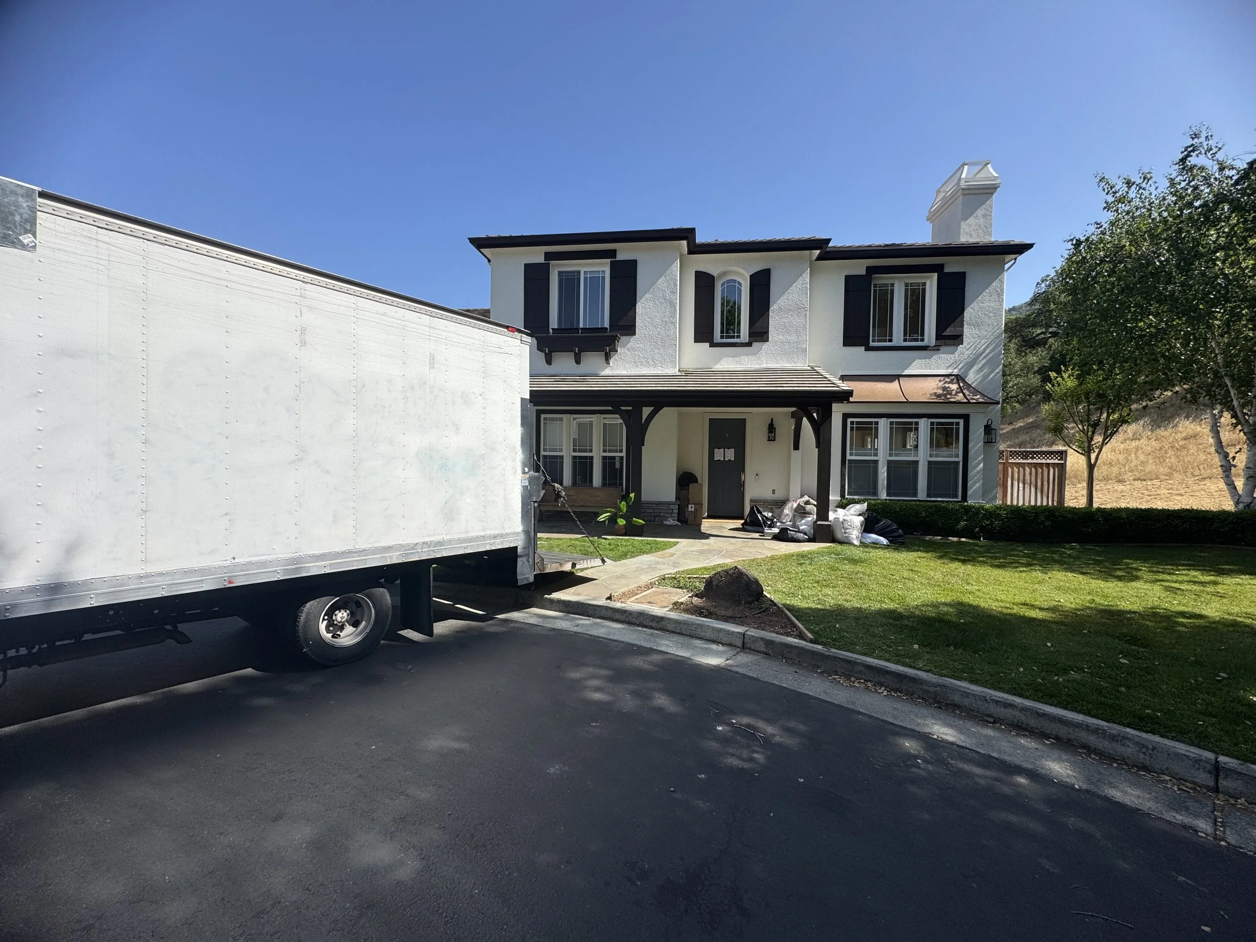 Modern building with wooden and white exterior walls and large glass window, set against a mountainous landscape with grass and plants in the foreground.