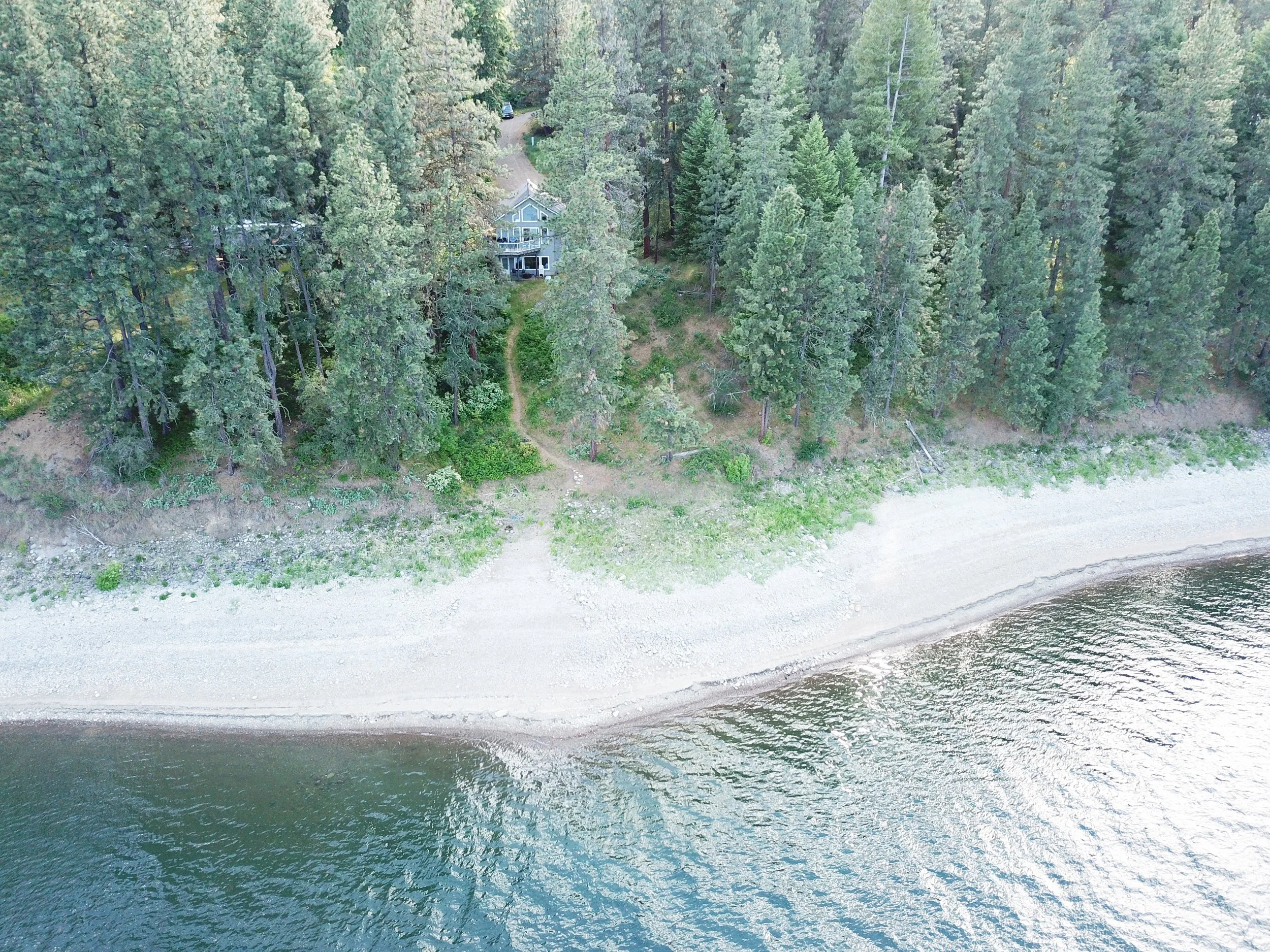 Aerial view of 2122 North Port Flat Creek on Lake Roosevelt, with a secluded waterfront home, dense pine forest and rocky beach.