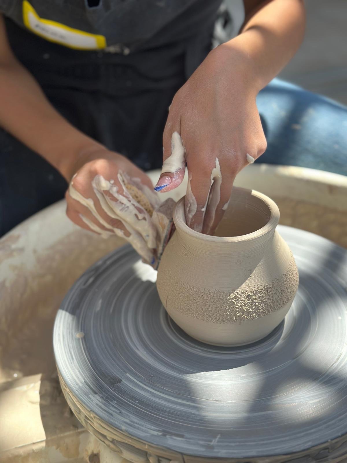 Person shaping a clay vase on a pottery wheel, with clay on their hands.