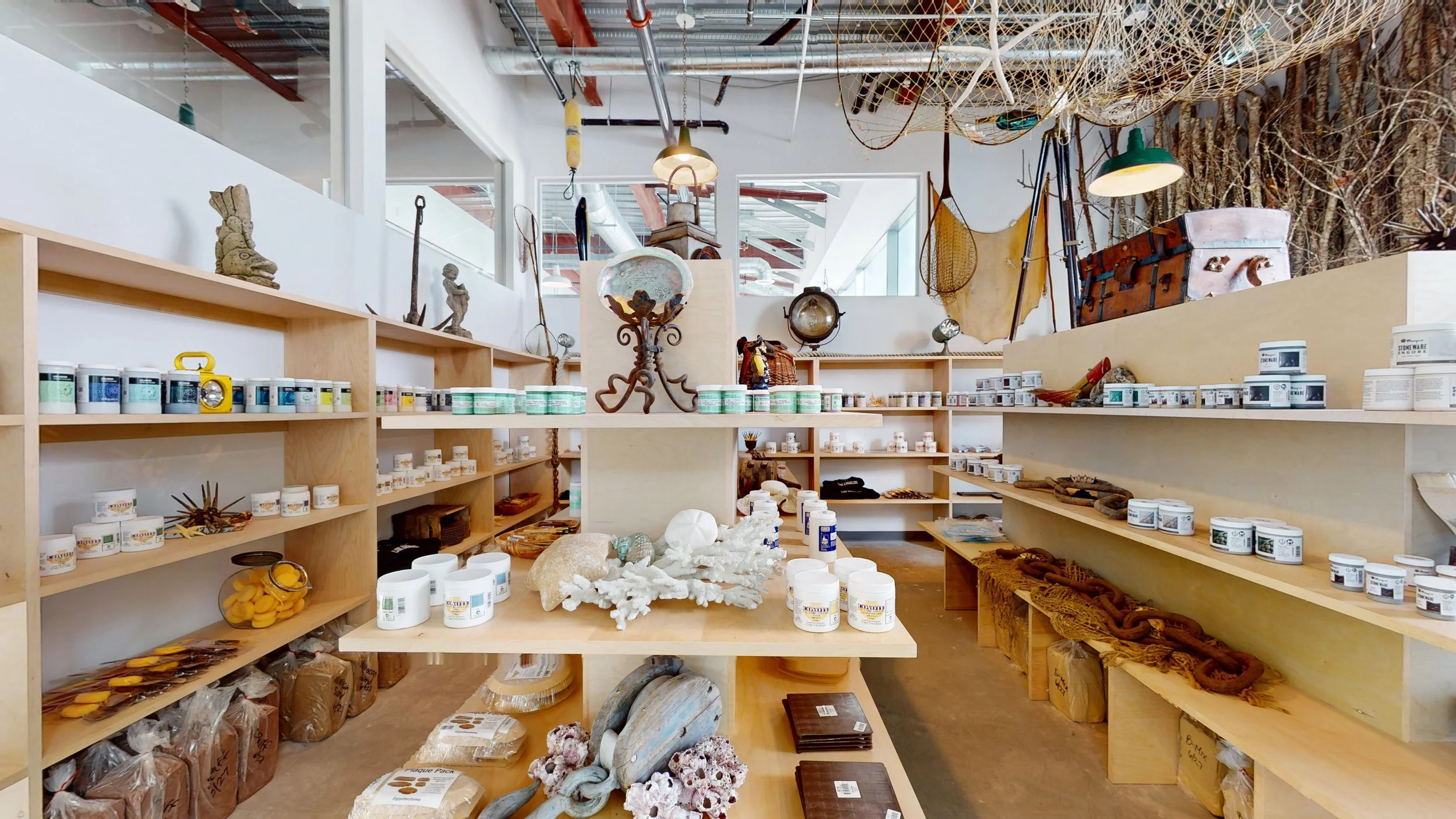 Interior of a store with wooden shelves displaying various items, including candles, decorations, and nautical-themed objects, with nautical netting and artifacts hanging from the ceiling.