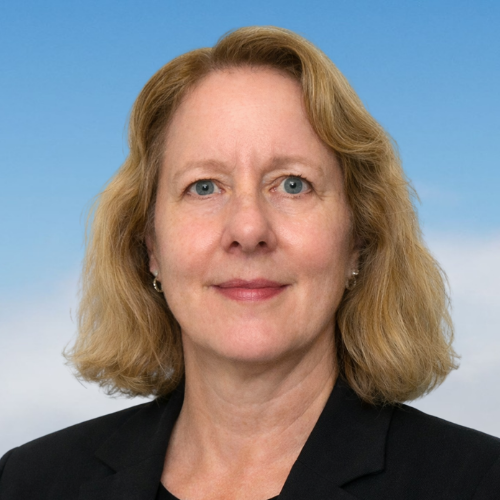 Close-up portrait of a woman with shoulder-length blonde hair, blue eyes, and fair skin against a blue sky with some clouds.