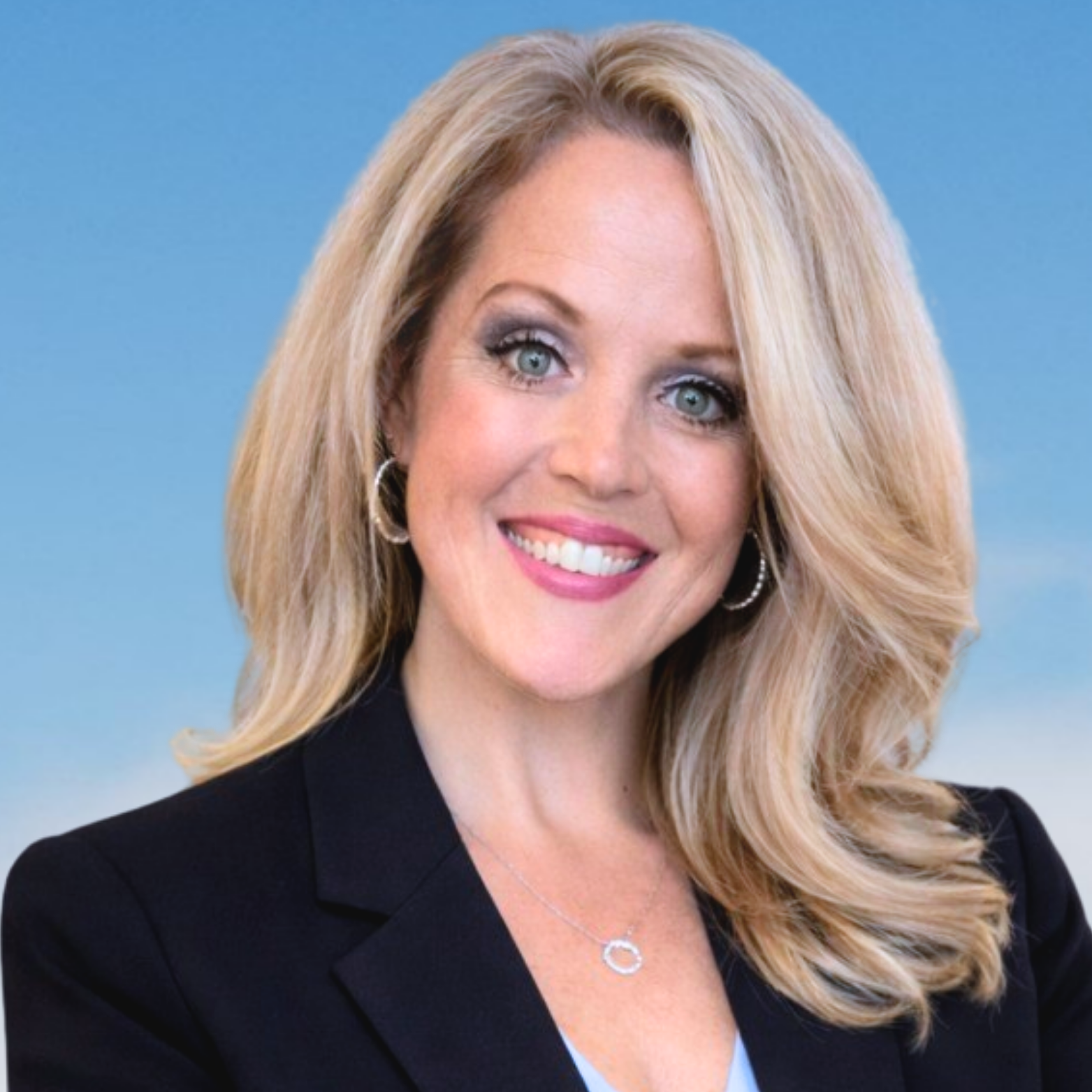 A smiling woman with blonde hair, wearing a black blazer and hoop earrings, against a blue sky background.