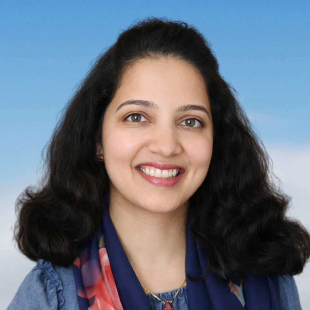 A woman with long, curly dark hair smiling in front of a blue sky background.