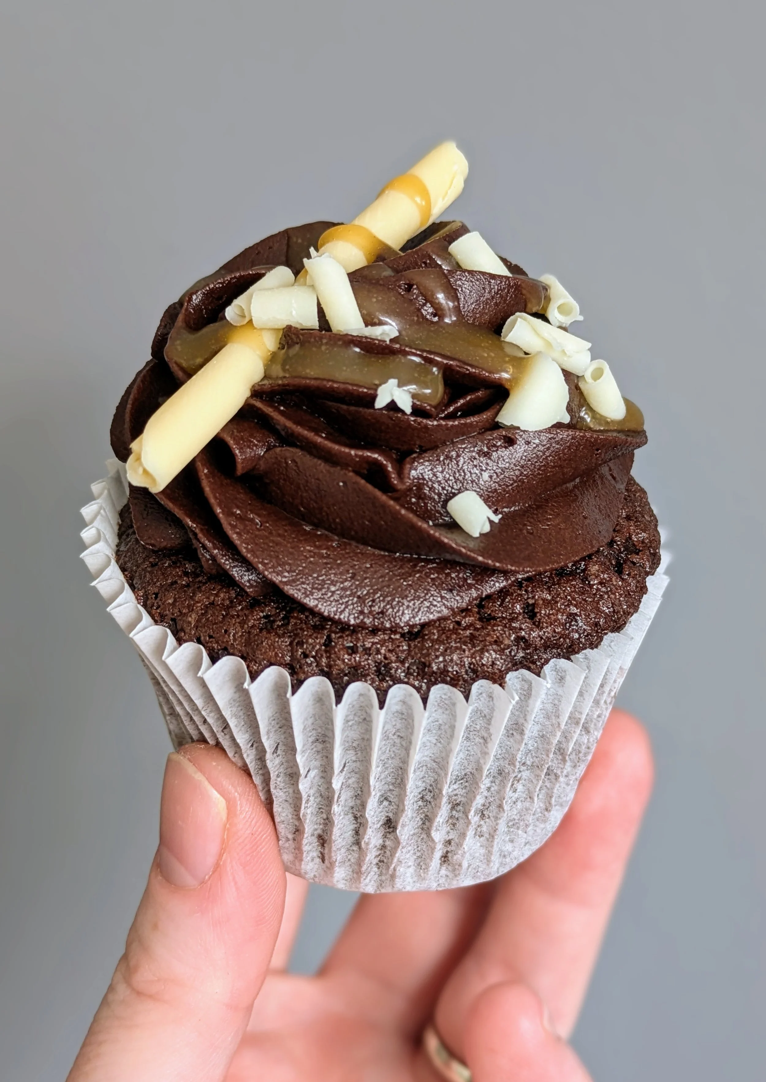 Chocolate cupcake with swirled chocolate frosting topped with caramel and white chocolate curls.