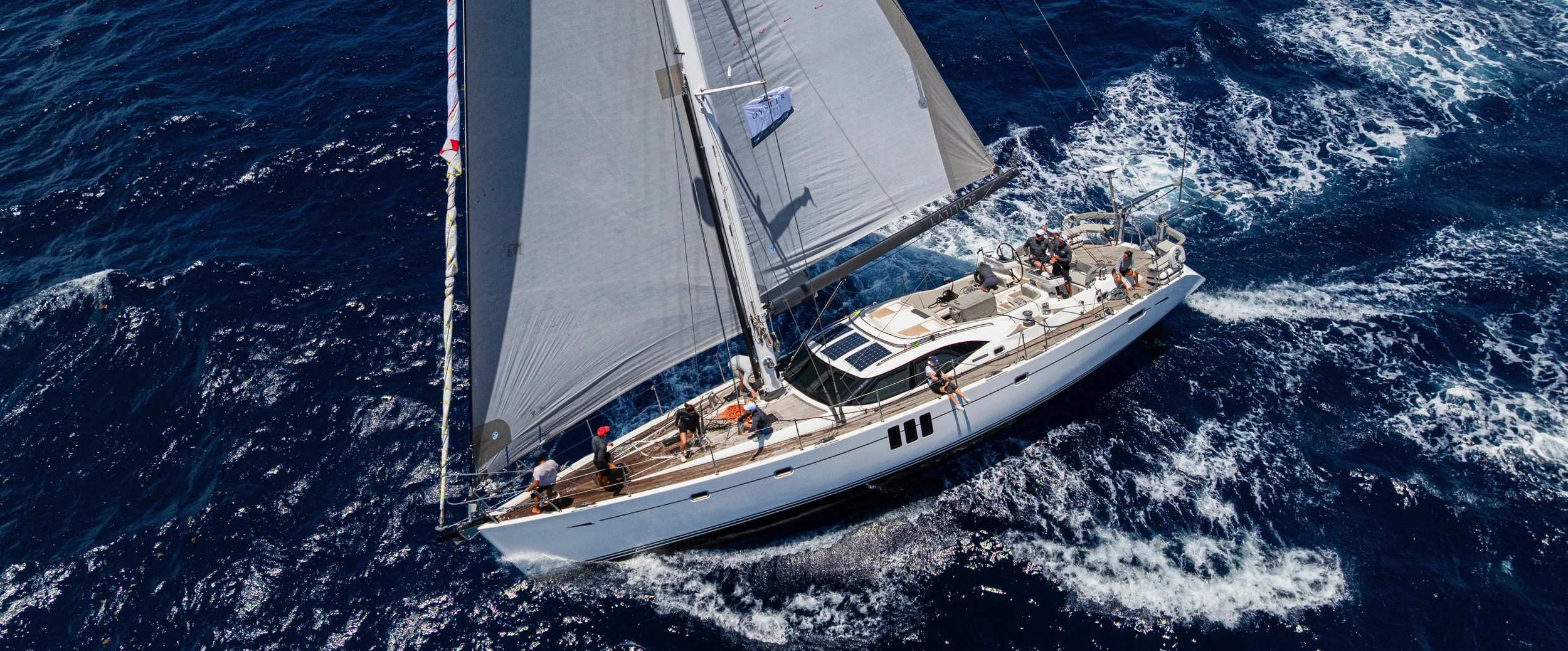 Aerial view of a sailboat with several people onboard sailing on the open ocean.