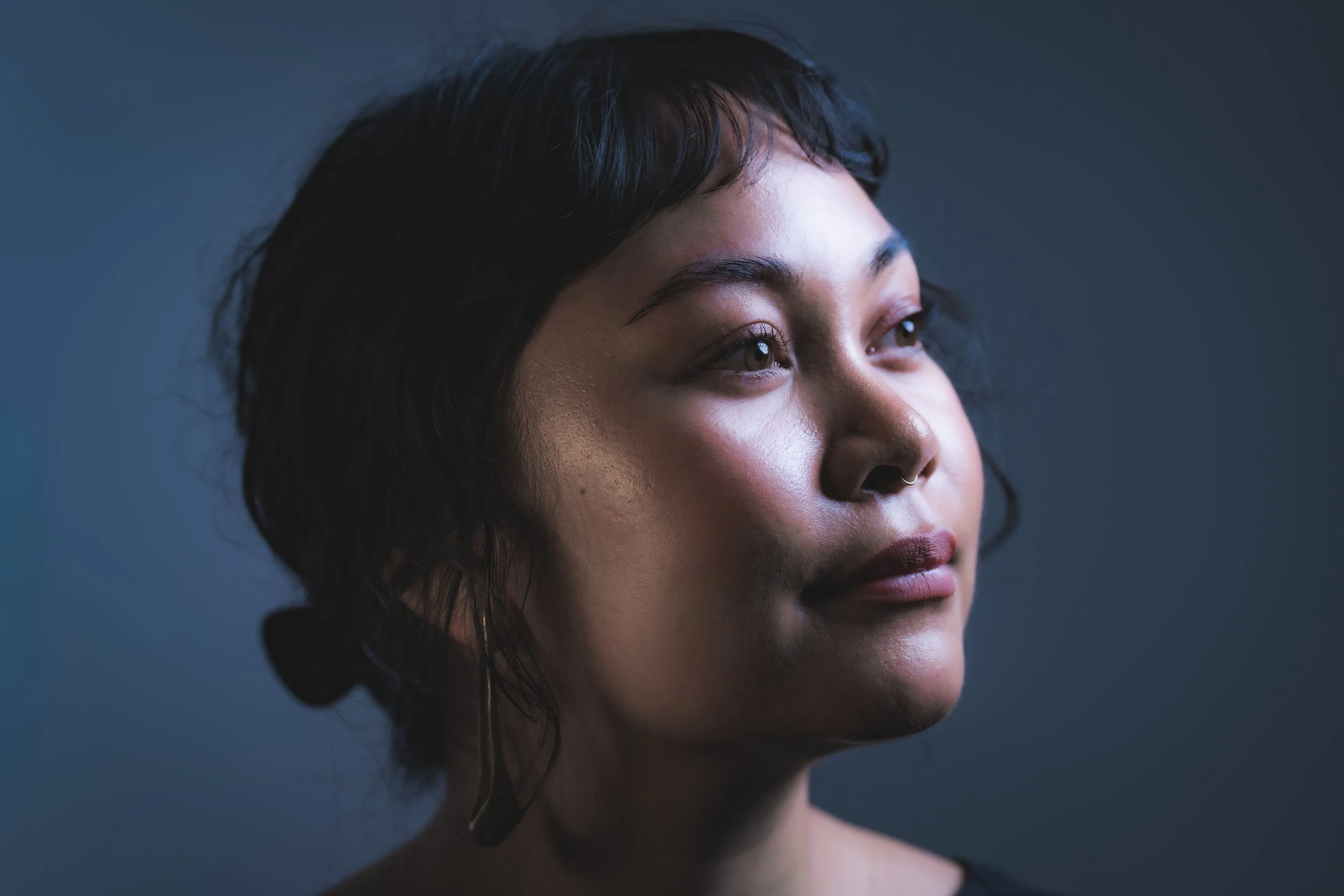A close-up portrait of a woman with short dark hair, wearing hoop earrings, looking off into the distance with a calm expression.