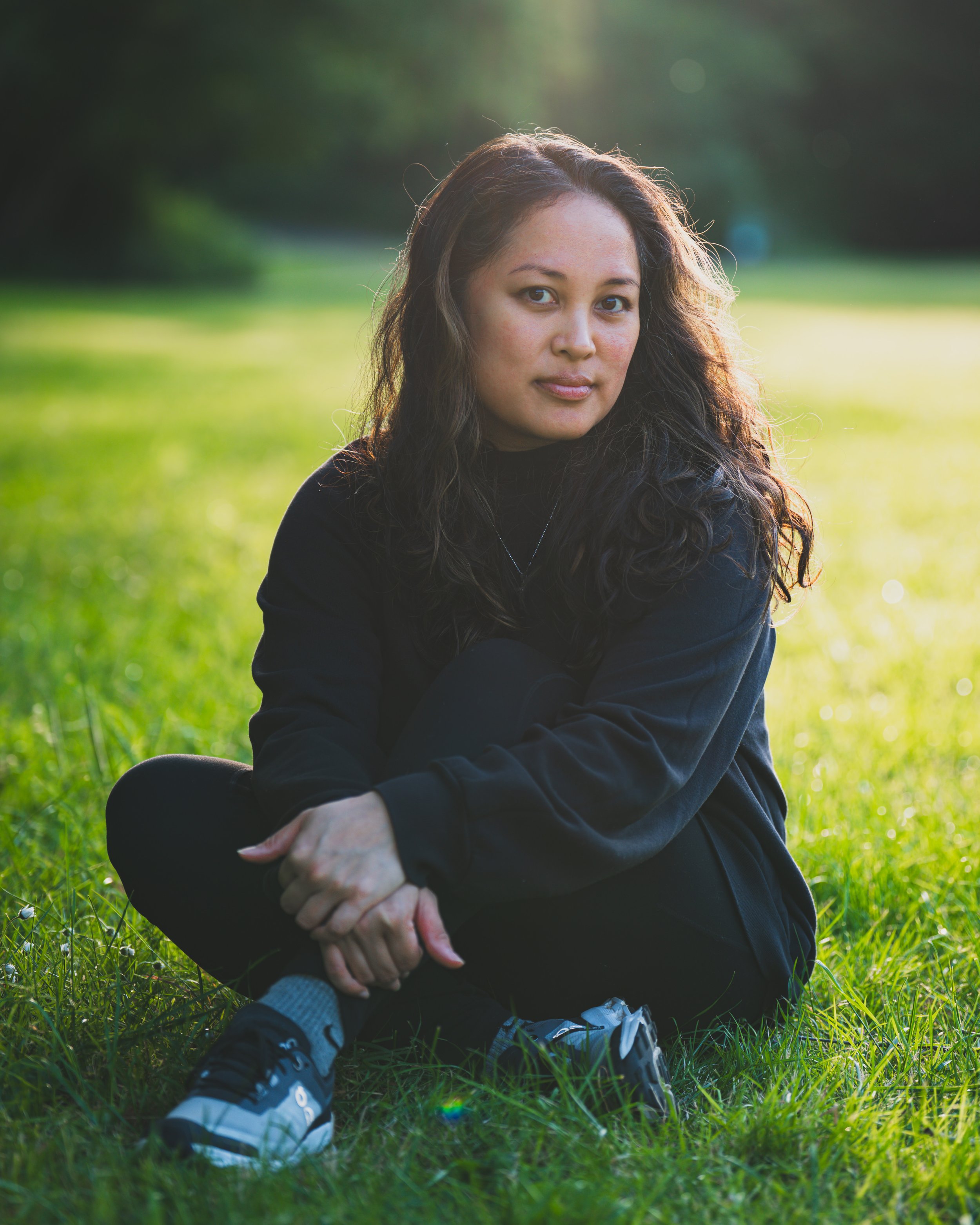 A woman sitting cross-legged on the grass in a park during sunset.
