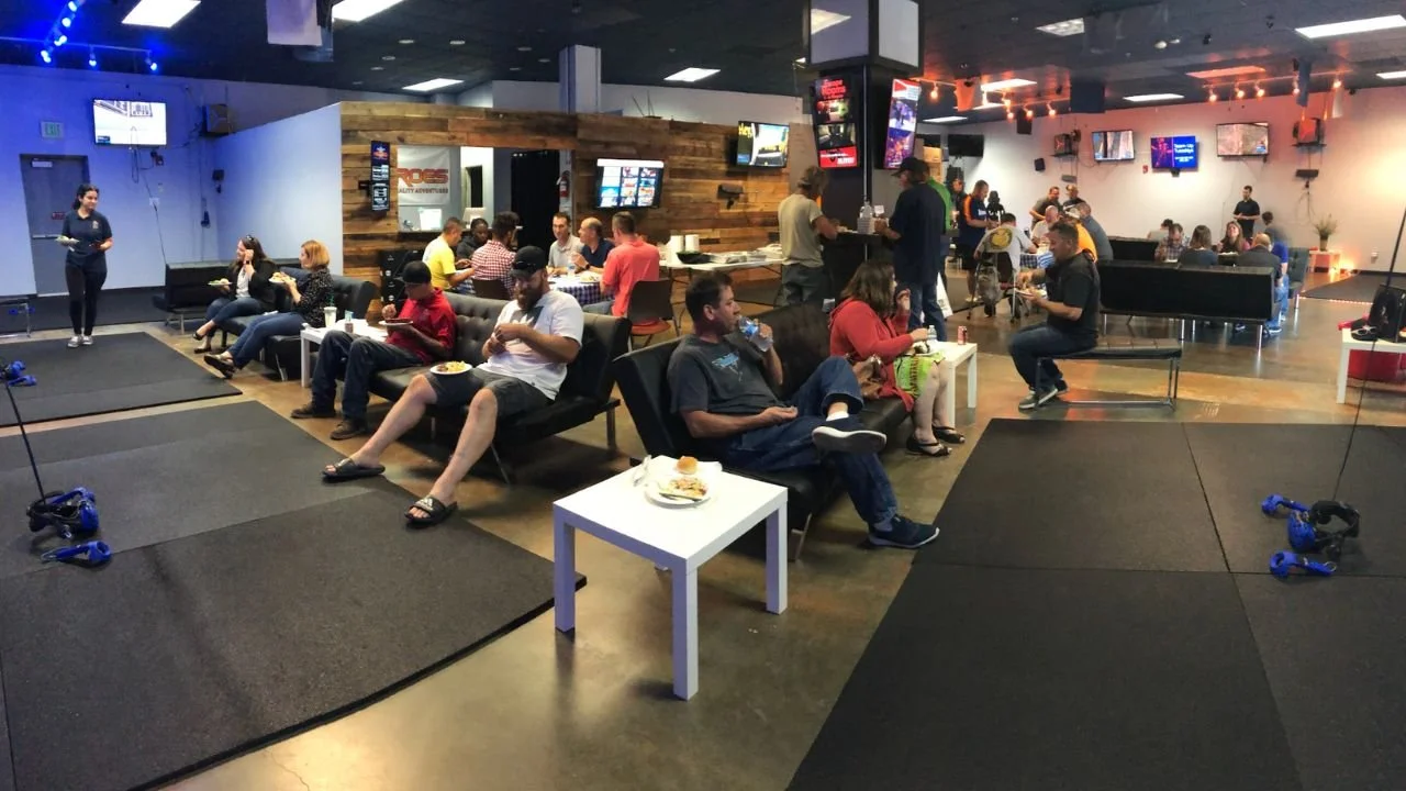 People relaxing and eating in a spacious virtual reality arcade lounge with gaming stations around
