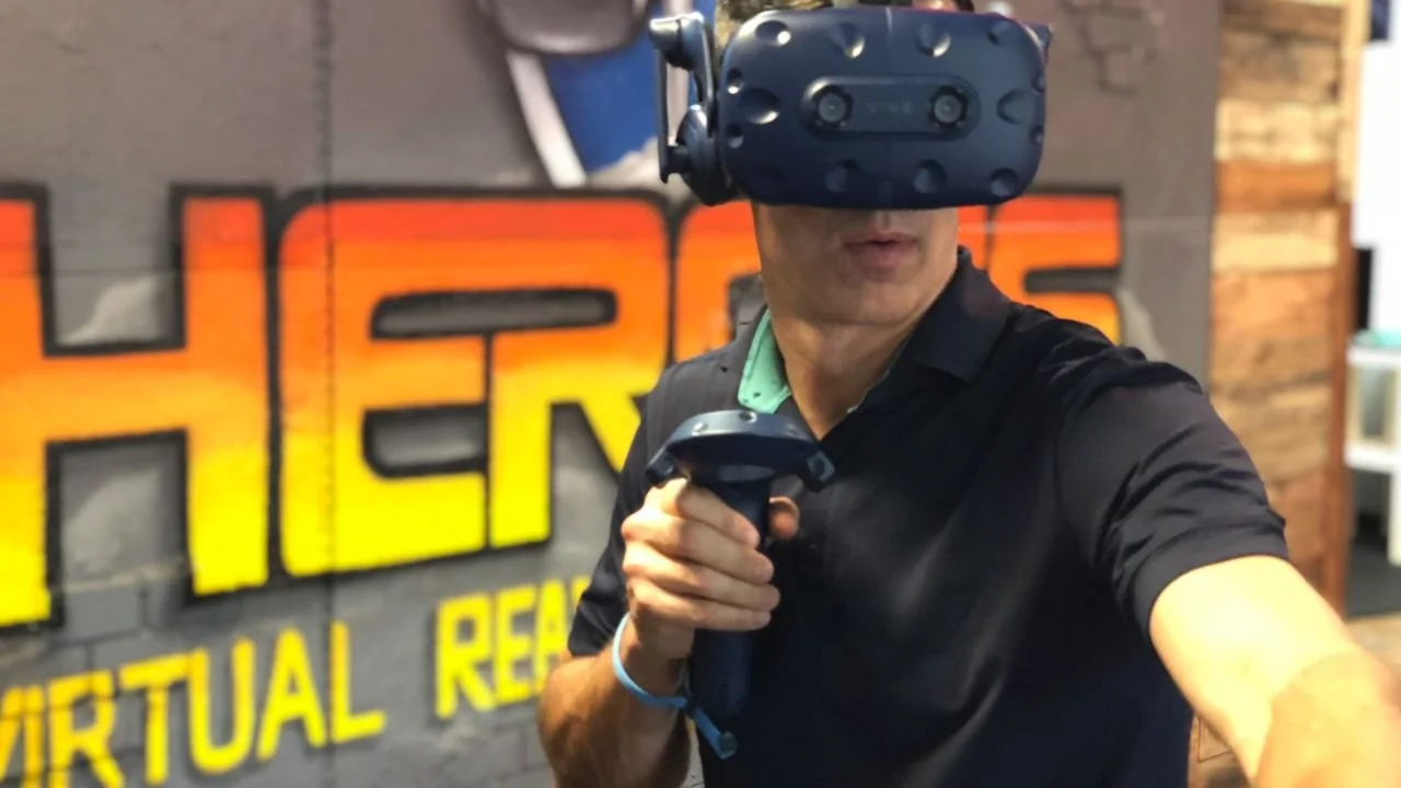 Participant using a VR headset and motion controllers during an interactive virtual reality game at HEROES VR Adventures.