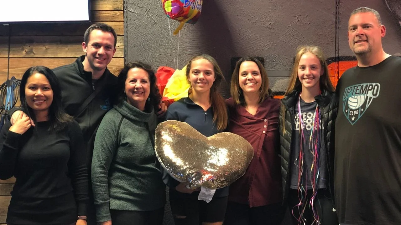 Group of friends and family celebrating a birthday with balloons and smiles inside an indoor entertainment venue
