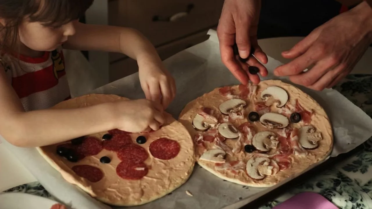 A child and adult making pizzas together, a hands-on culinary activity for indoor birthday party ideas.