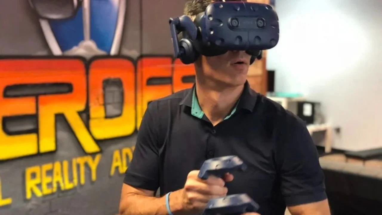 Man wearing a VR headset and holding controllers inside a virtual reality arcade.