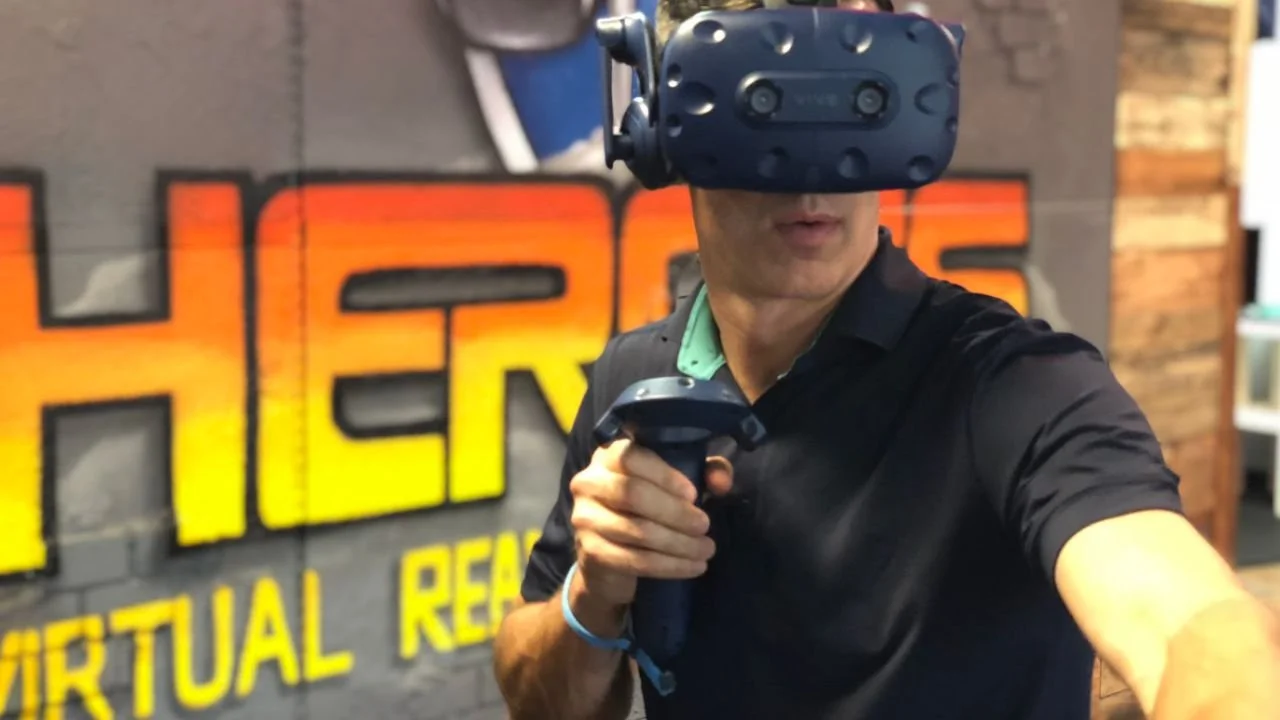 Player wearing a VR headset and extending motion controllers at HEROES VR Adventures.