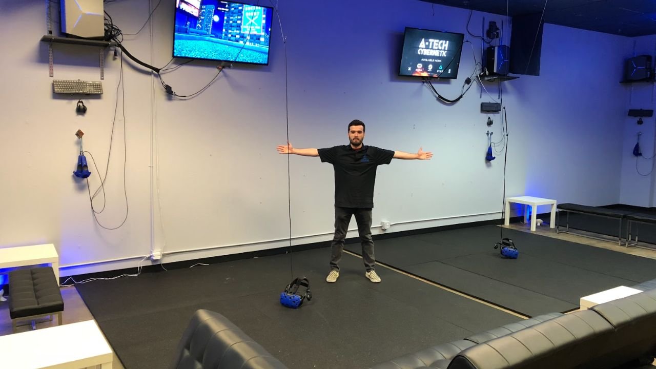 Man standing with arms wide in a spacious virtual reality gaming room with VR headsets and screens setup