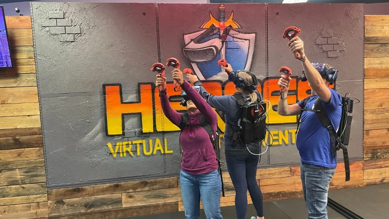Three people wearing VR headsets and using handheld controllers during a multiplayer virtual reality experience.