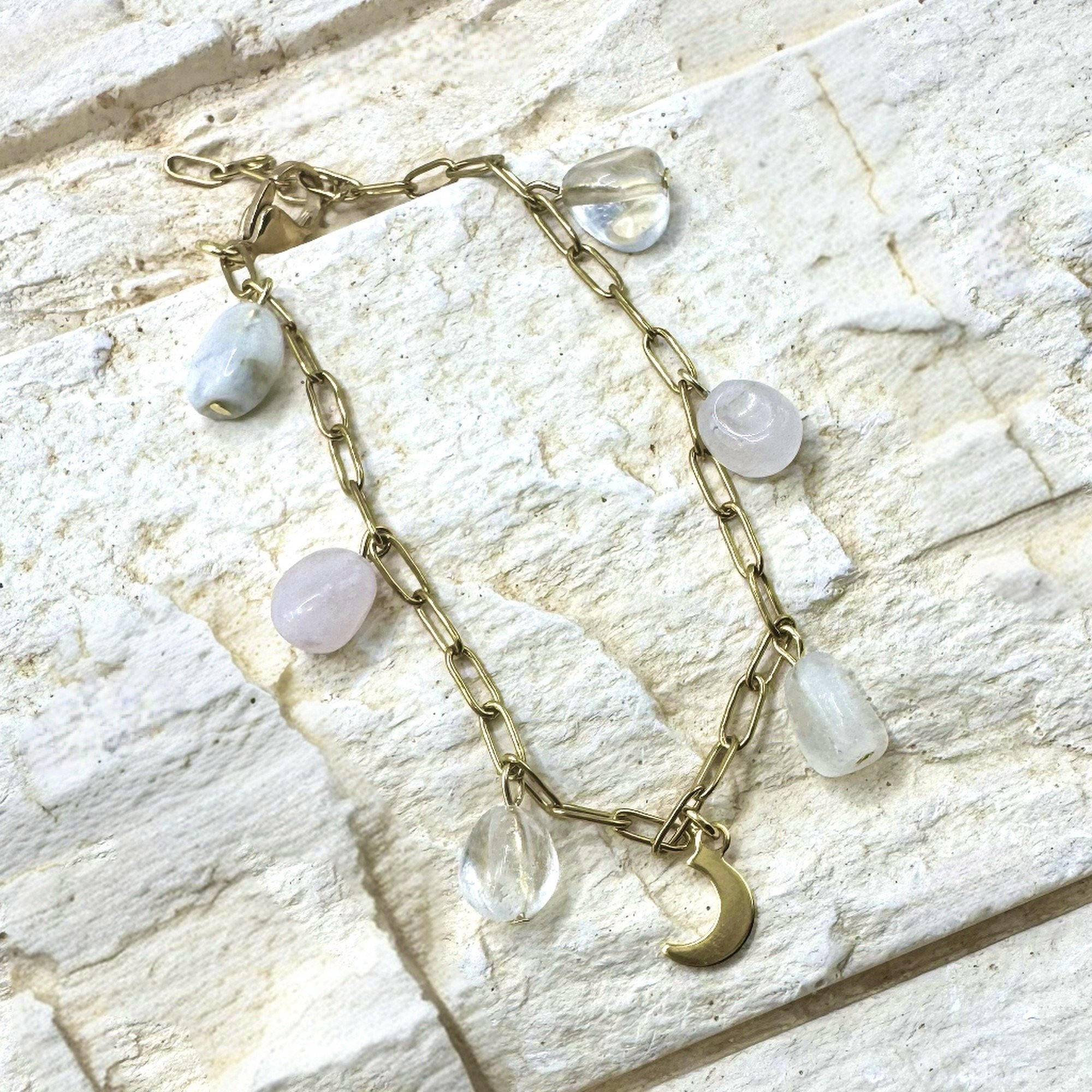 Eine goldene Kettenarmband mit weißen Perlen und Anhängern, darunter ein goldener Halbmondanten.