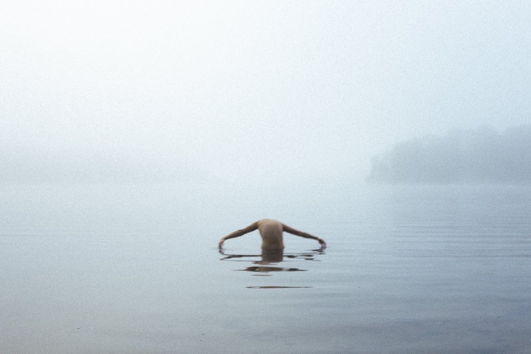 Person taucht in einem nebligen See unter.