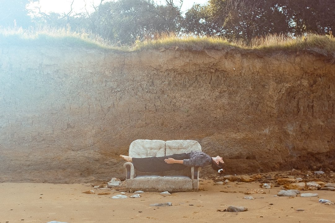 Person liegt auf einem Sofa in einer felsigen, sandigen Landschaft.