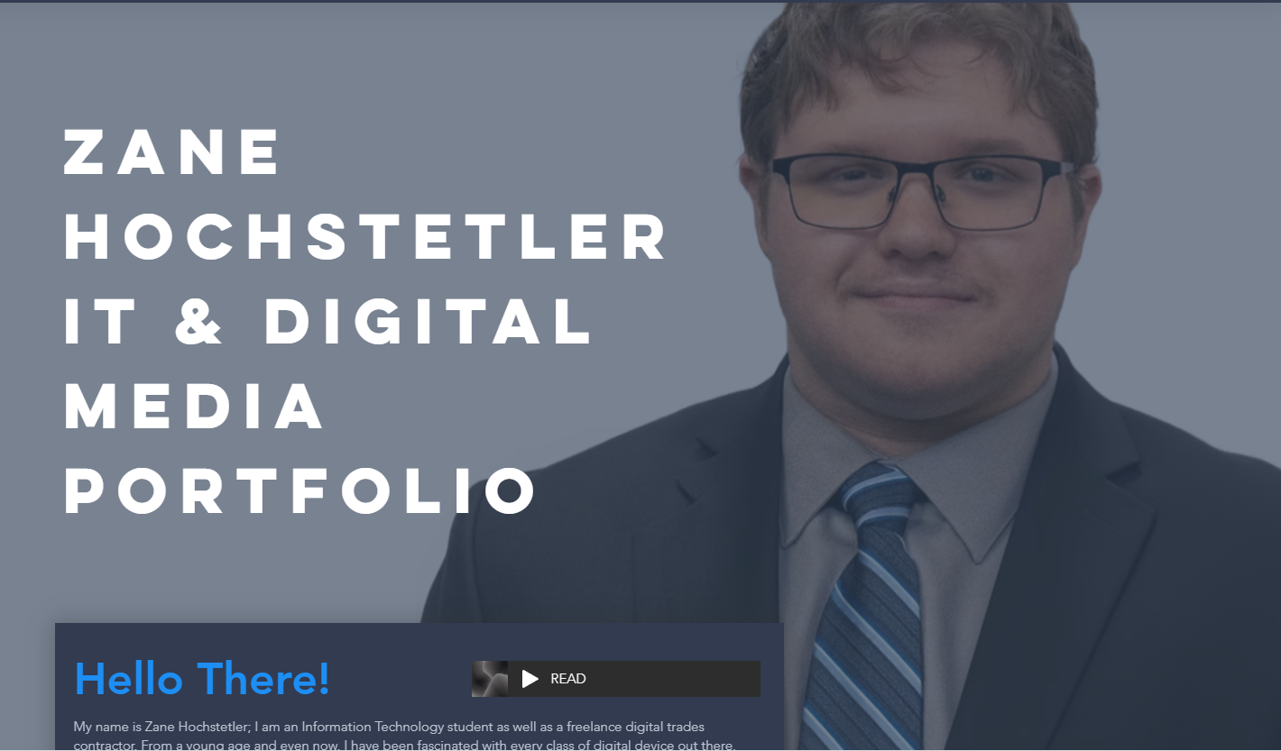 A professional portrait of Zane Hochstetler, an IT and digital media student, dressed in a business suit with a striped tie, wearing glasses, against a plain background.