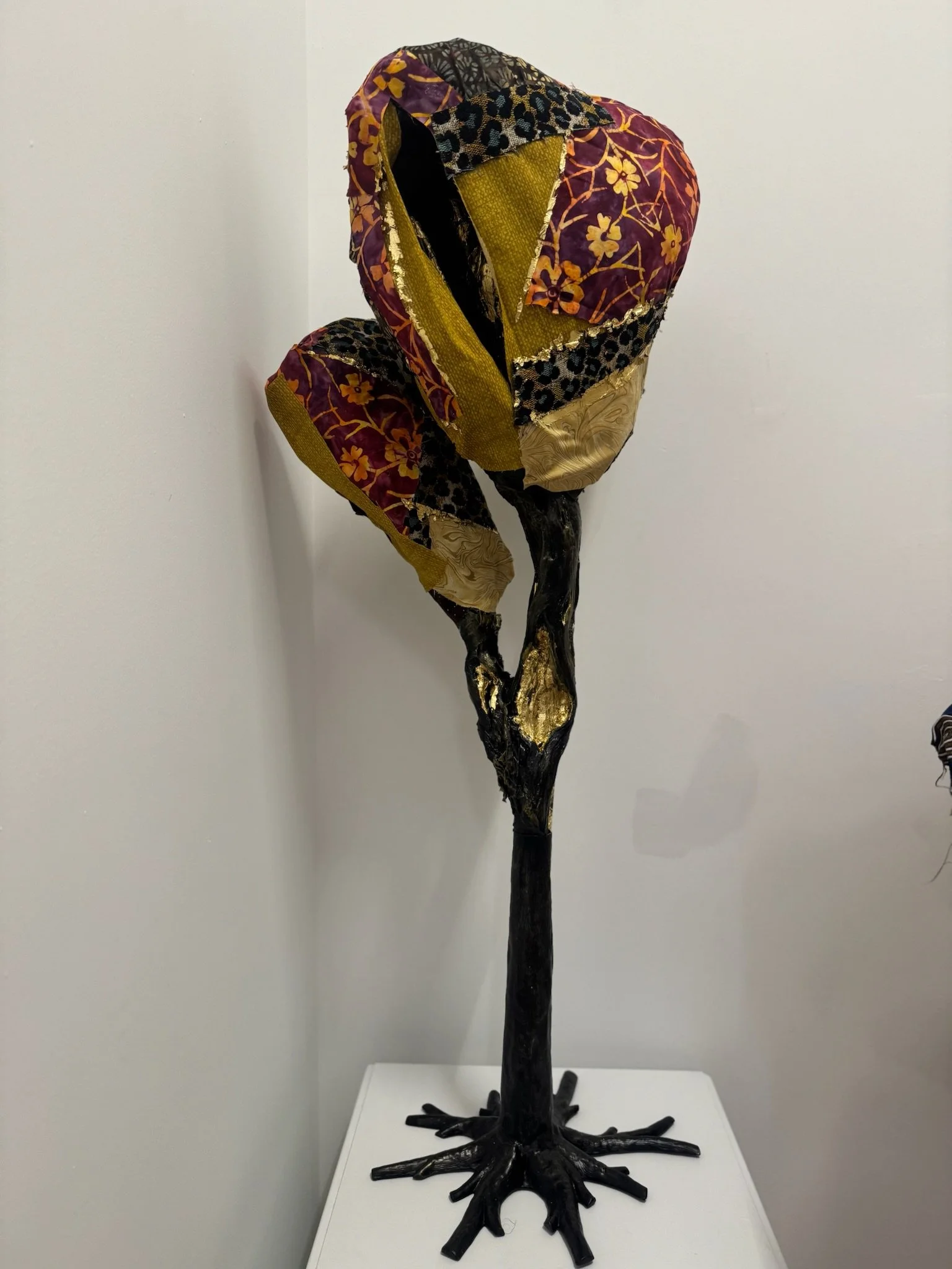 A sculpture of a tree with a black trunk and roots, with large, colorful, patterned leaves made of fabric or similar material.