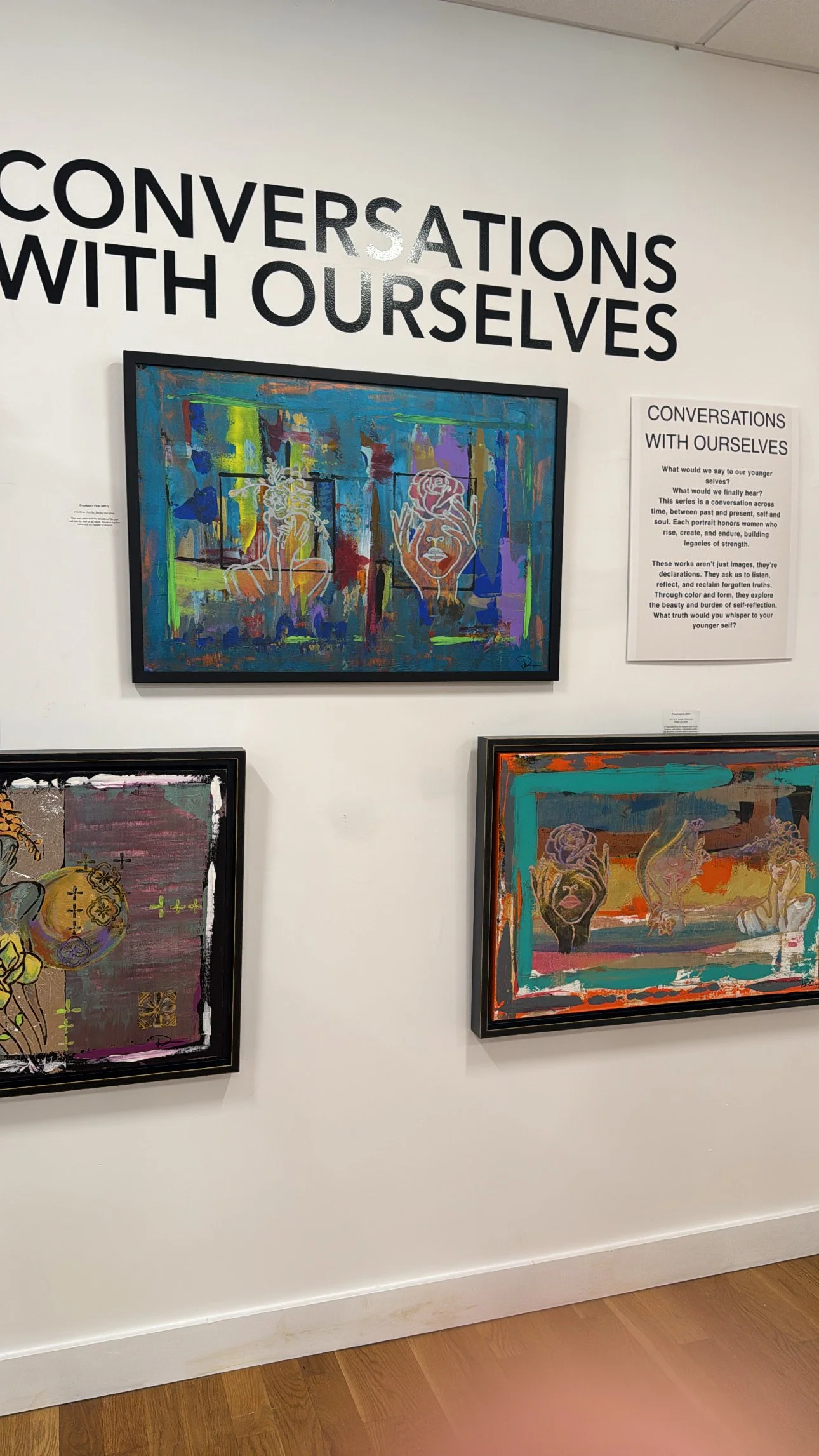 Three colorful abstract paintings on a gallery wall with a sign titled 'Conversations with Ourselves' and a description about introspective art.
