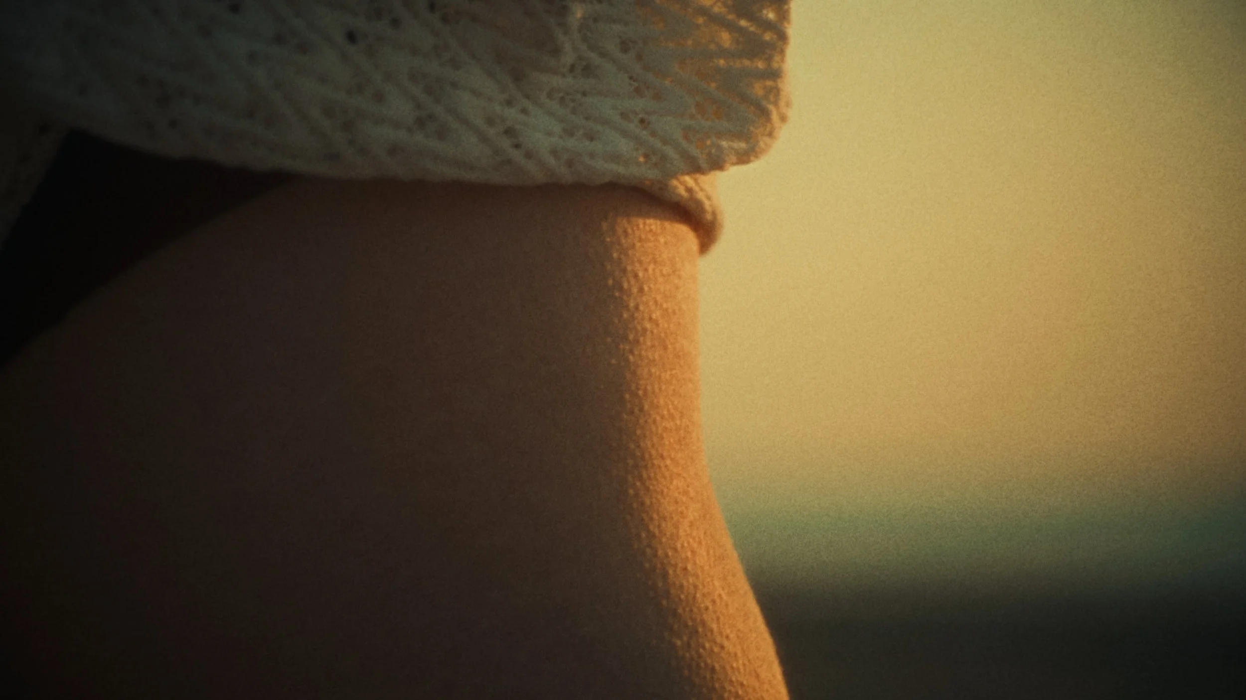 Close-up of a person's arm wearing a white lace sleeve, illuminated by warm sunlight, with a blurry background