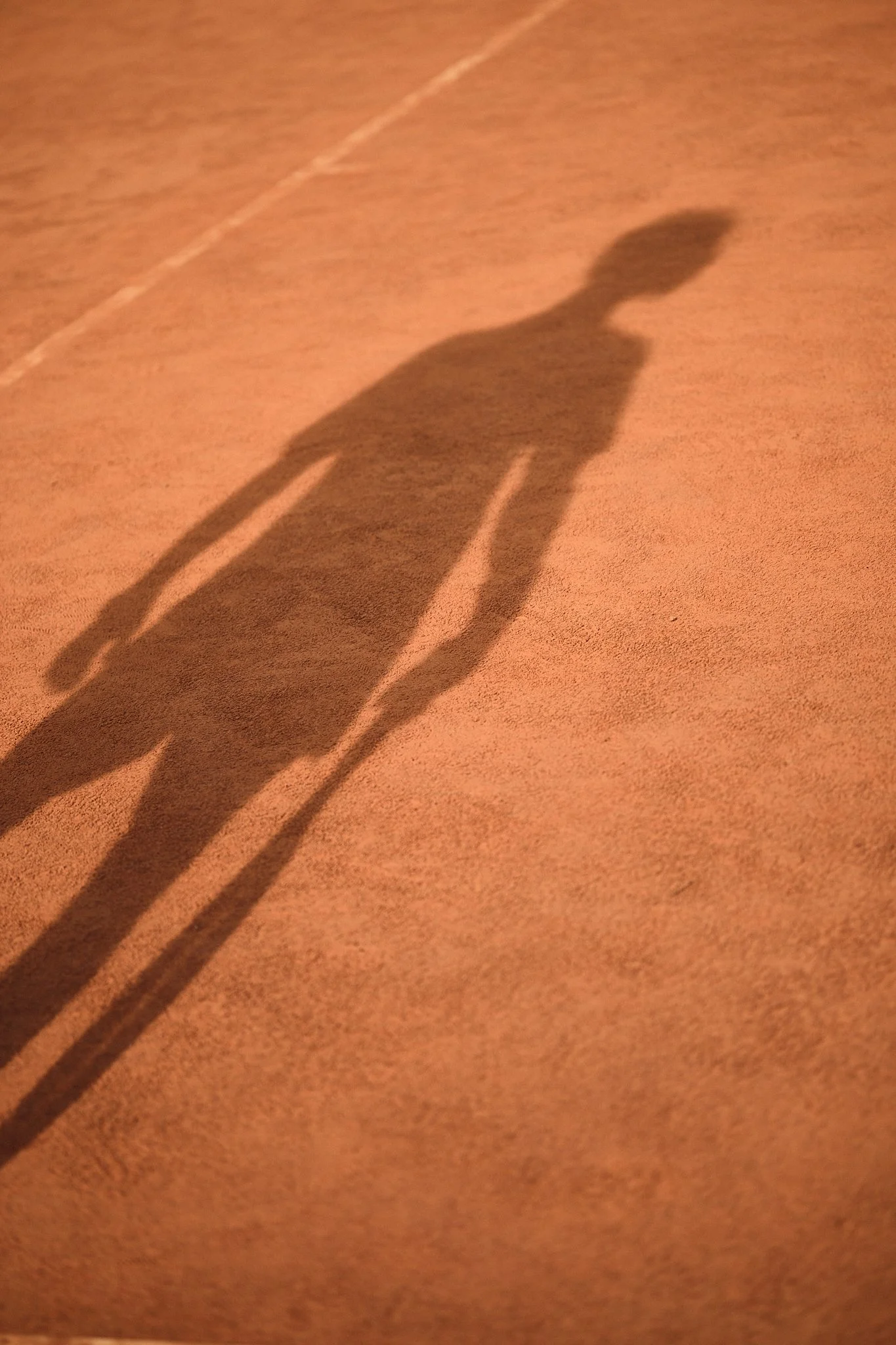Shadow of a person on a clay court surface.