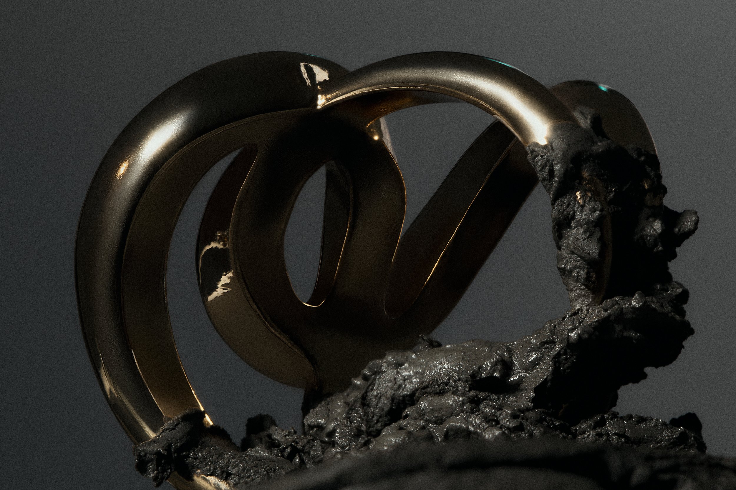 A metallic Bitcoin symbol partially encased in black and gray volcanic rock.