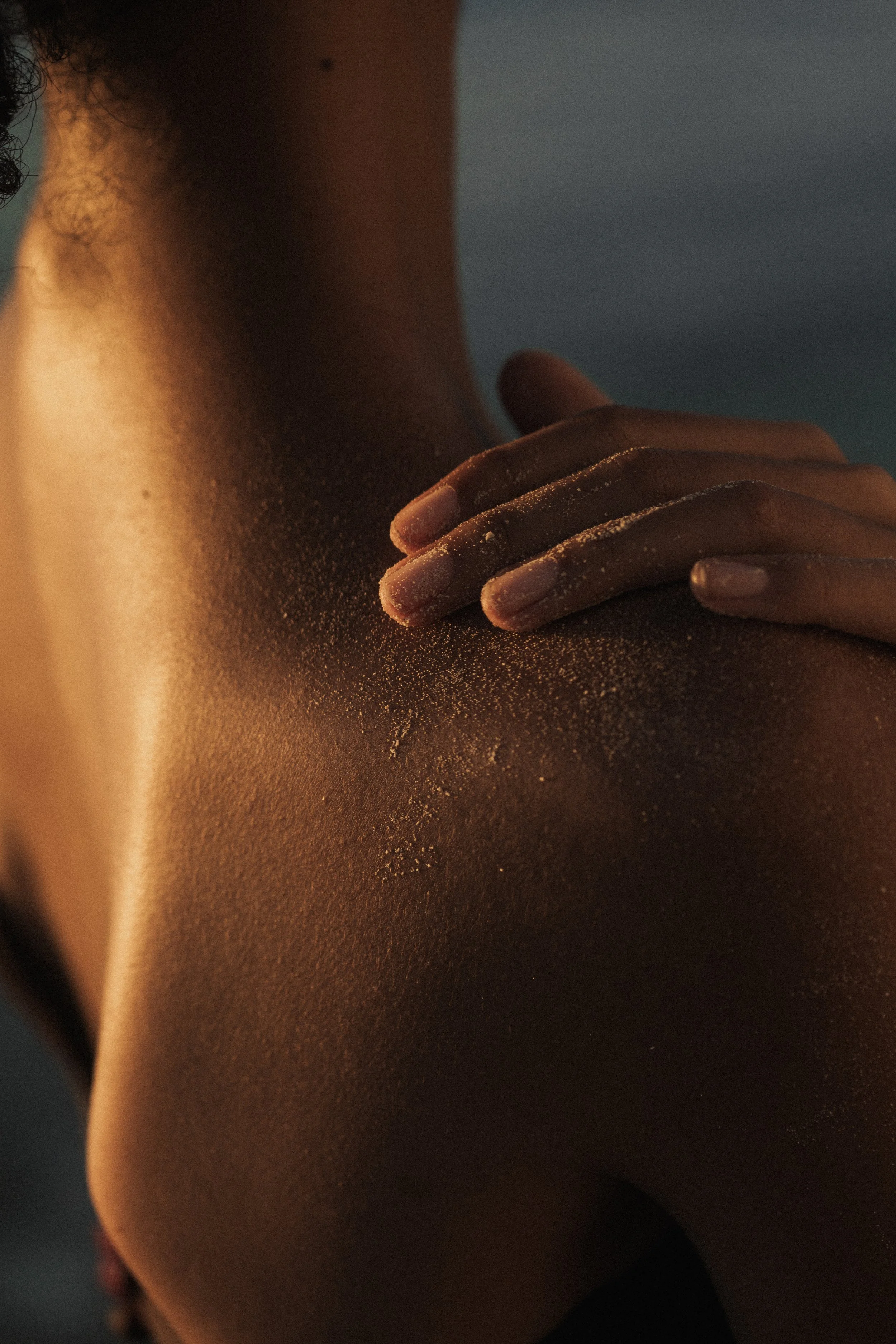 Close-up of a person's shoulder and hand with sand on their skin.