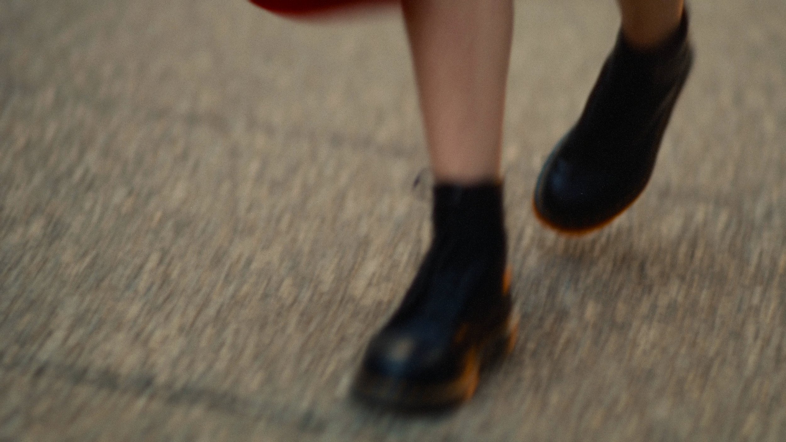A close-up of a person's legs and feet wearing black shoes and black socks, walking on a beige carpeted floor.