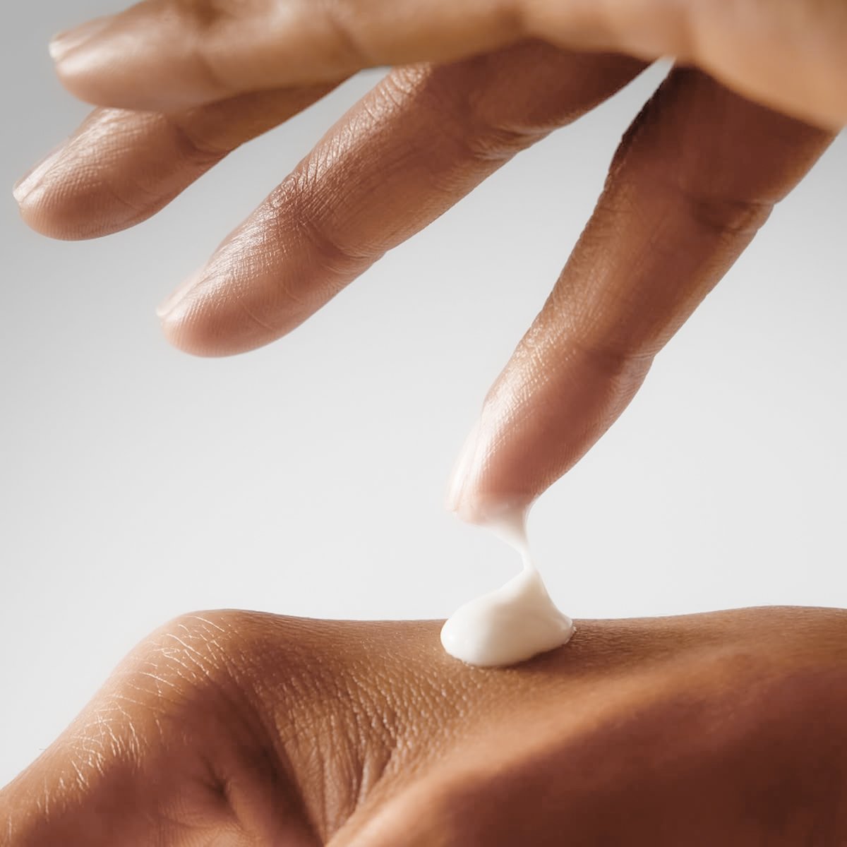 Close-up of a person's hand squeezing lotion onto their skin.