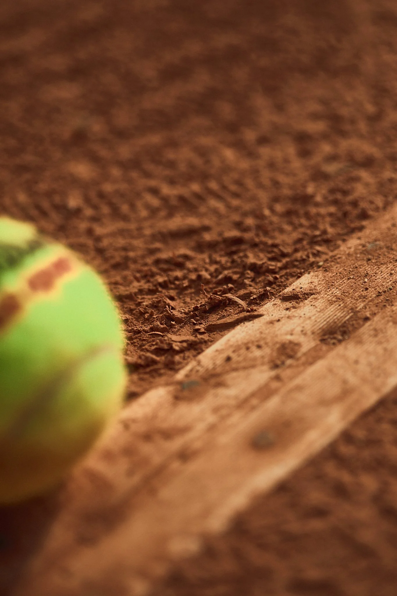 Close-up of clay court a partial ball in the foreground and a piece of wood on the right side.