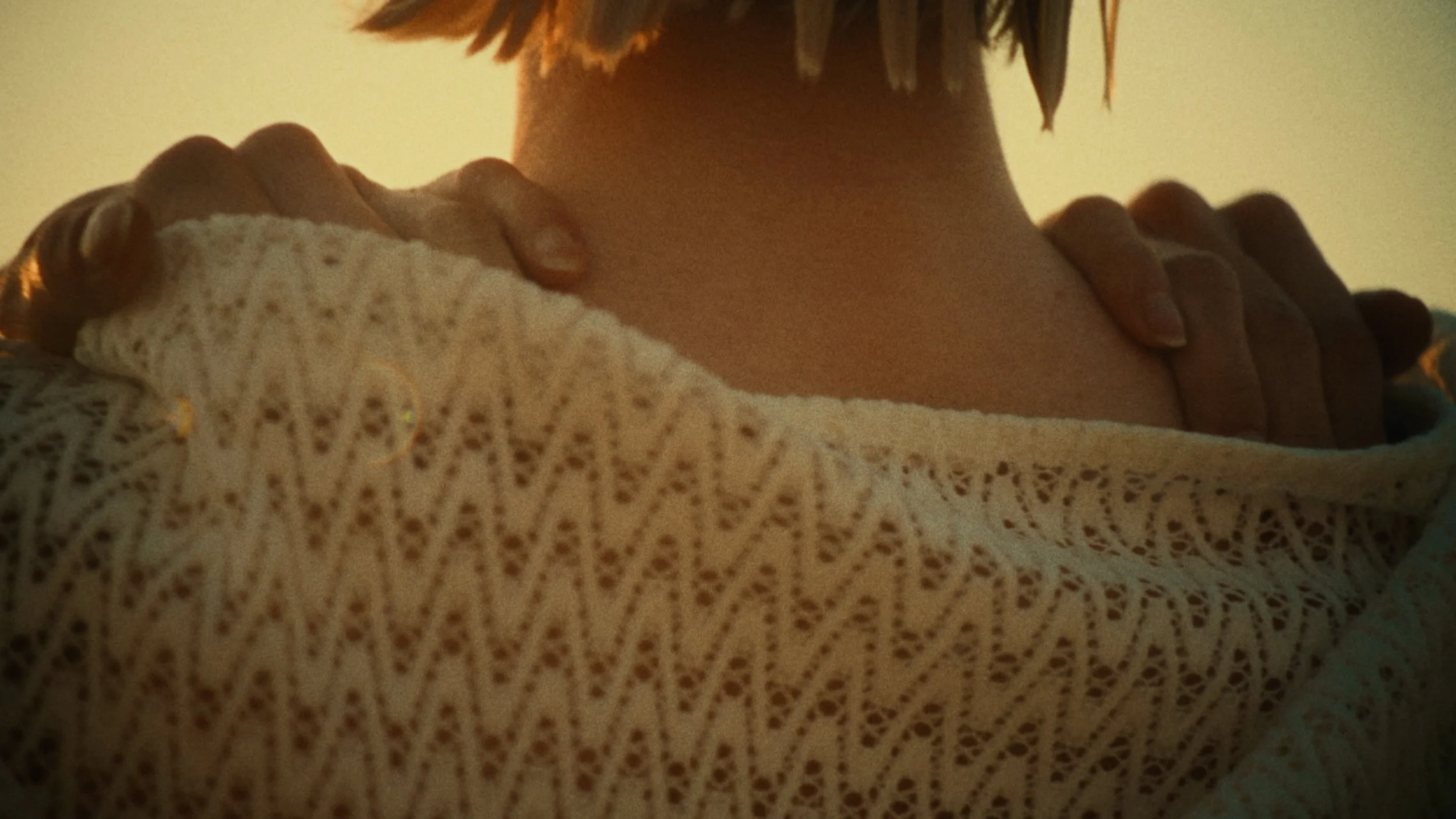 Person holding their shoulder, wearing a patterned beige shirt, with short hair visible on the left side.