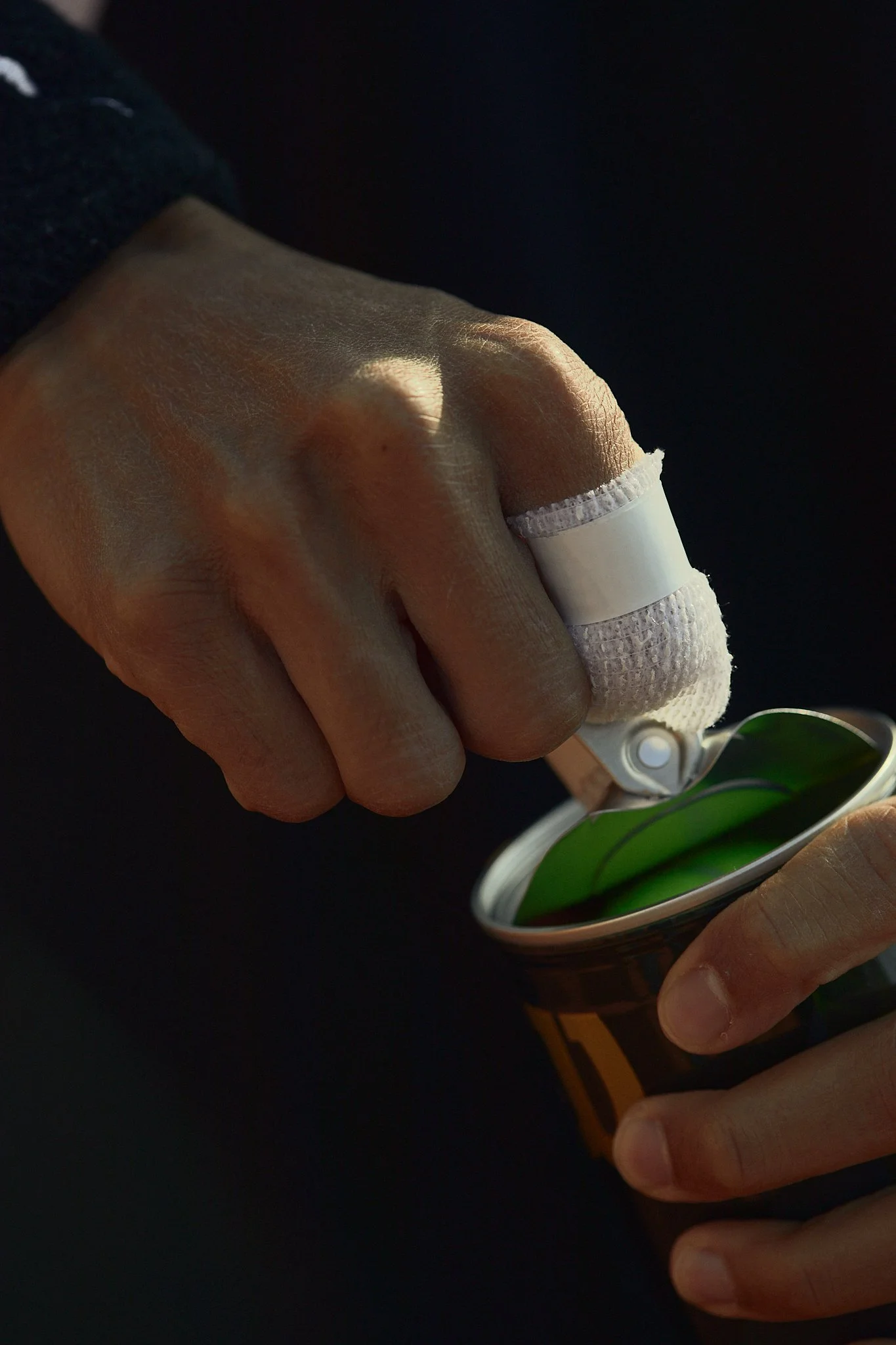 Close-up of a person's hand with a bandaged thumb, opening a can of tennis balls using a pull tab.