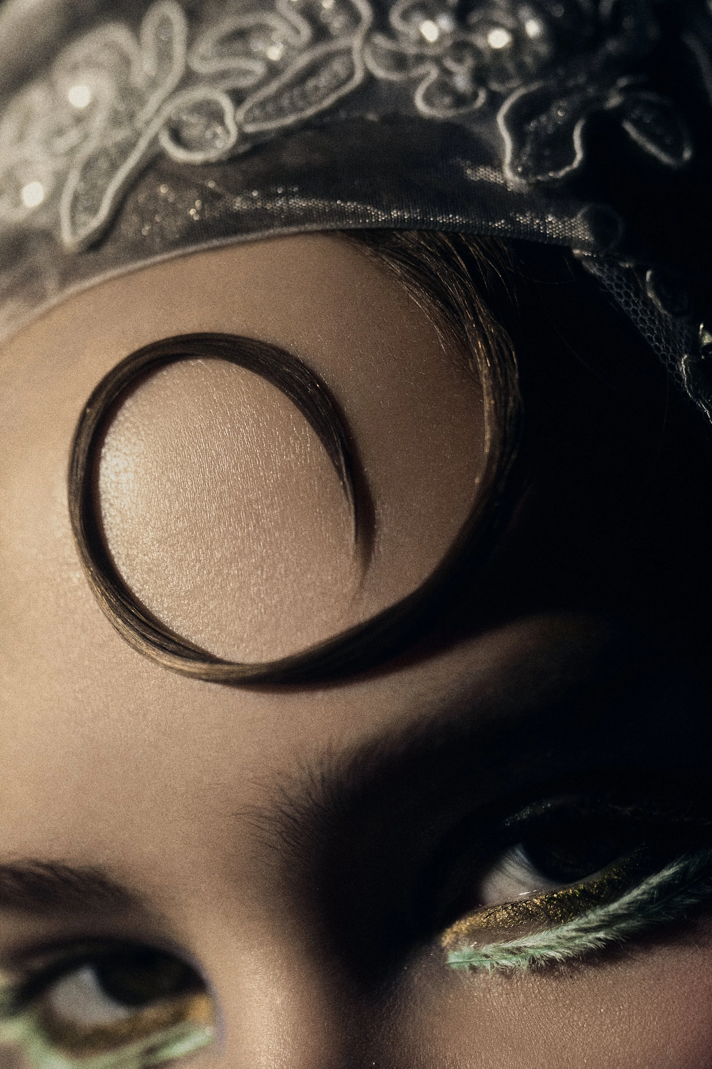 Close-up of a person's face with geometric eye makeup and a metallic head covering, showing part of the eyes and forehead.