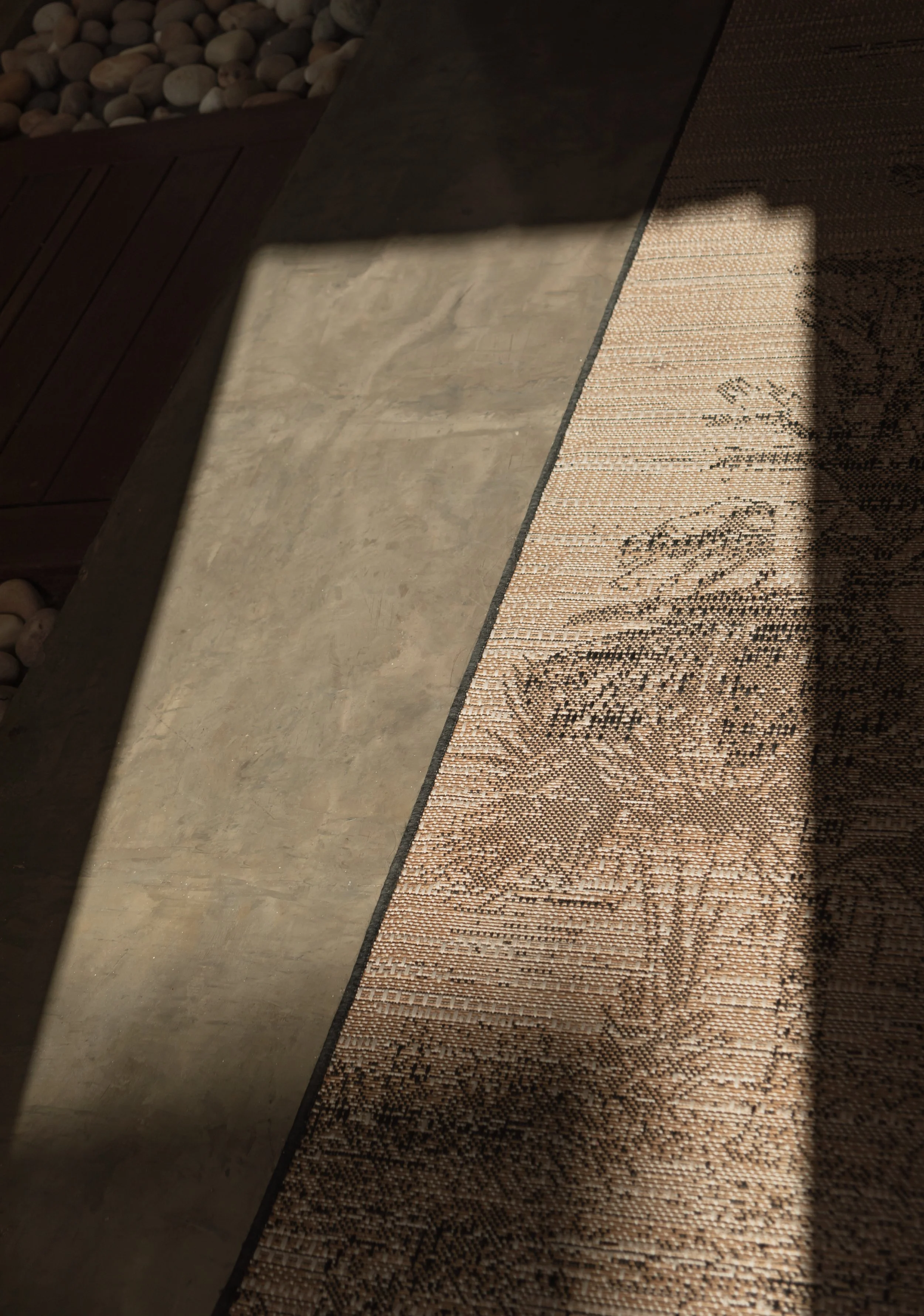 Close-up of a textured rug on a hard surface floor with shadow cast across it.