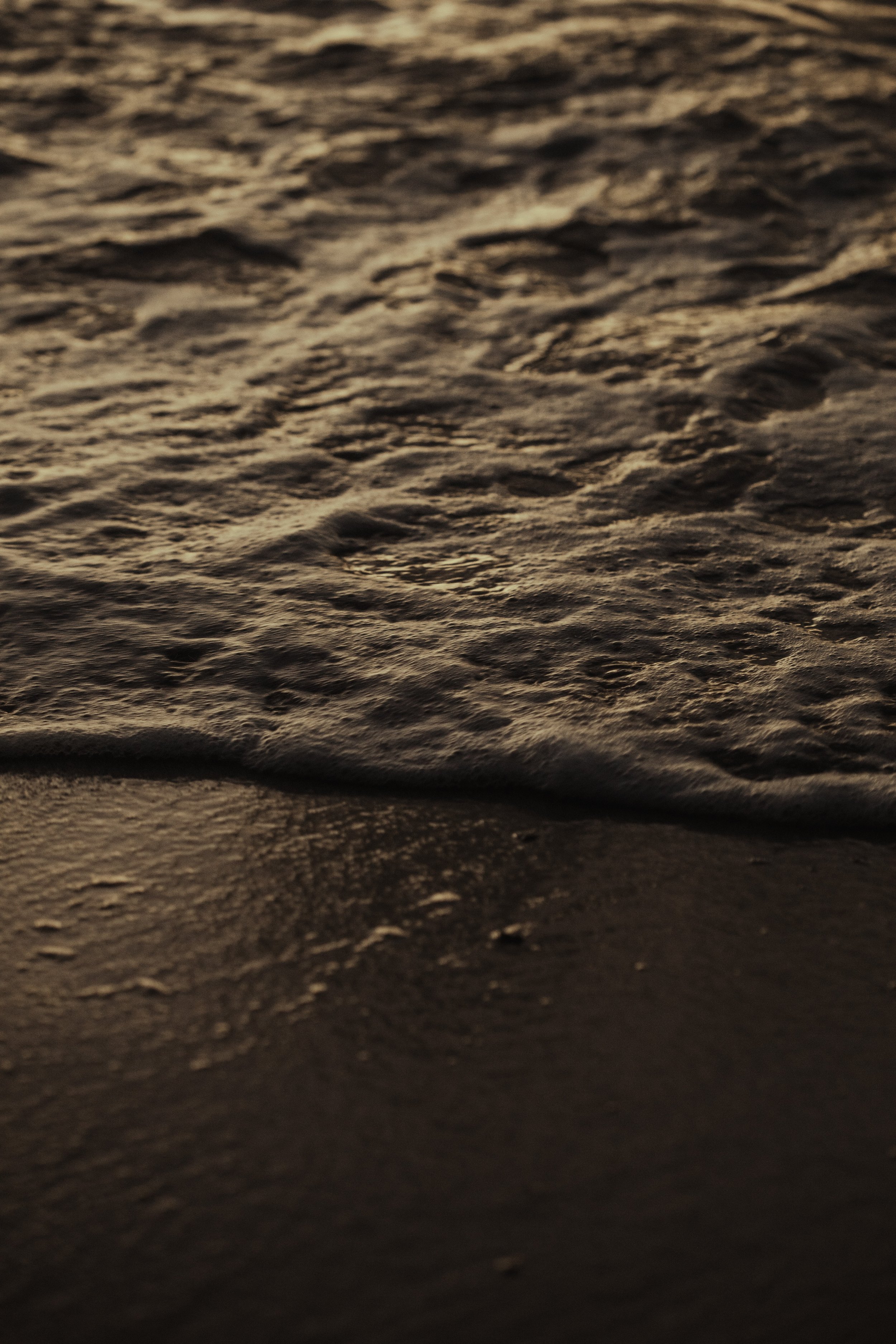 Close-up of sand and gentle ocean waves at sunset.