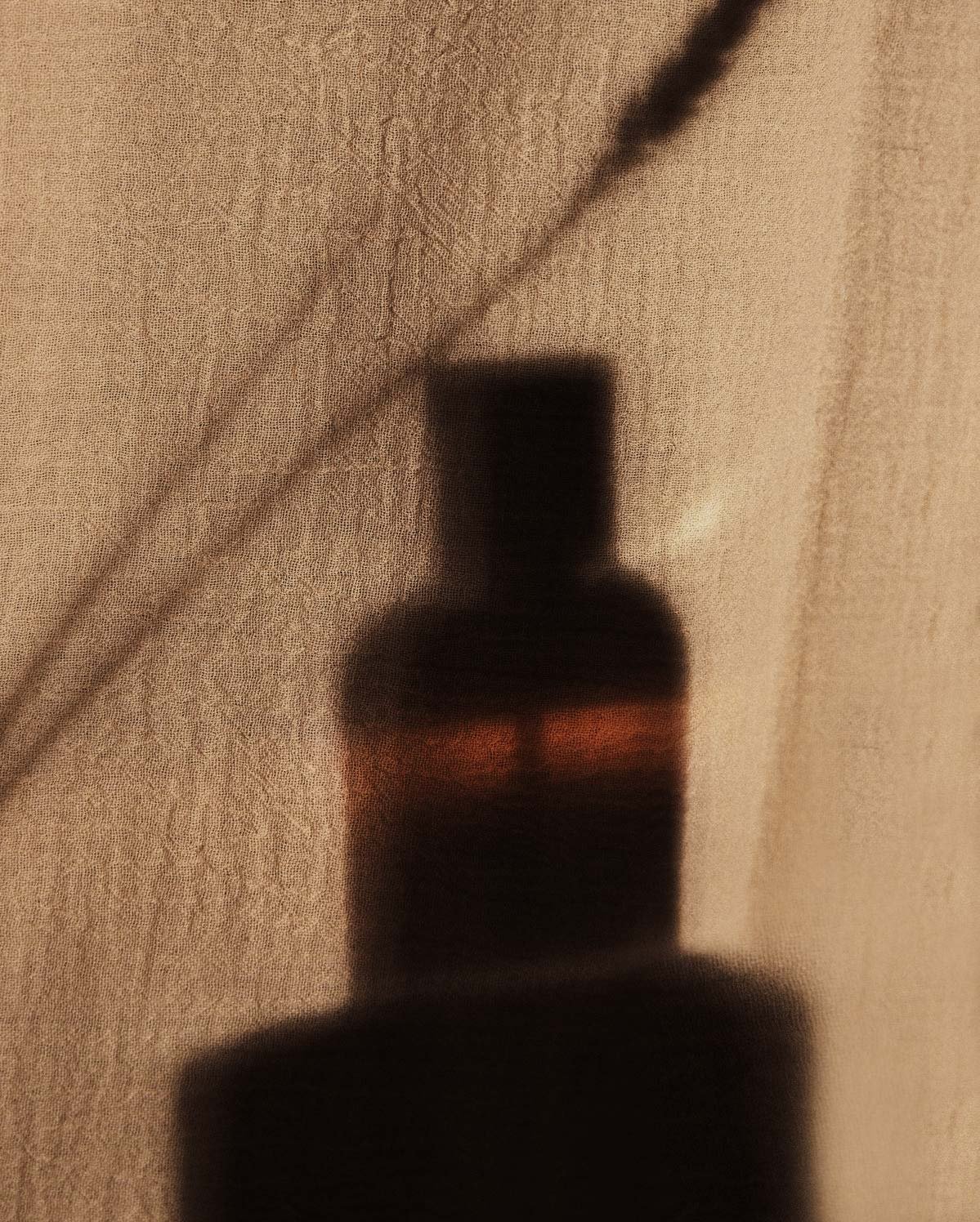 Blurred reflection of a perfum, with a blurred background and a textured surface.