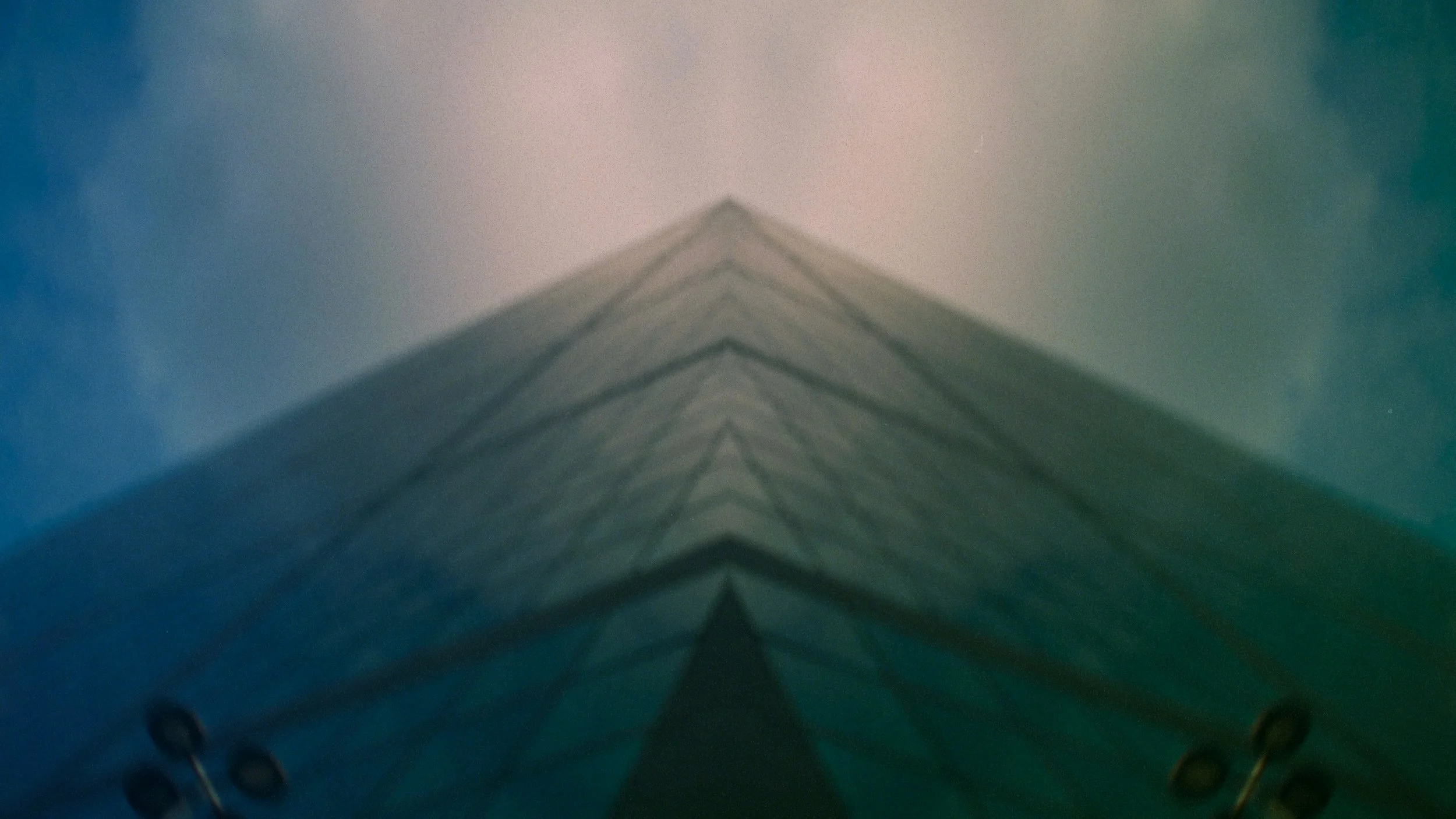 Looking up at a tall building from below with a symmetrical, pointed roof and sky in the background.