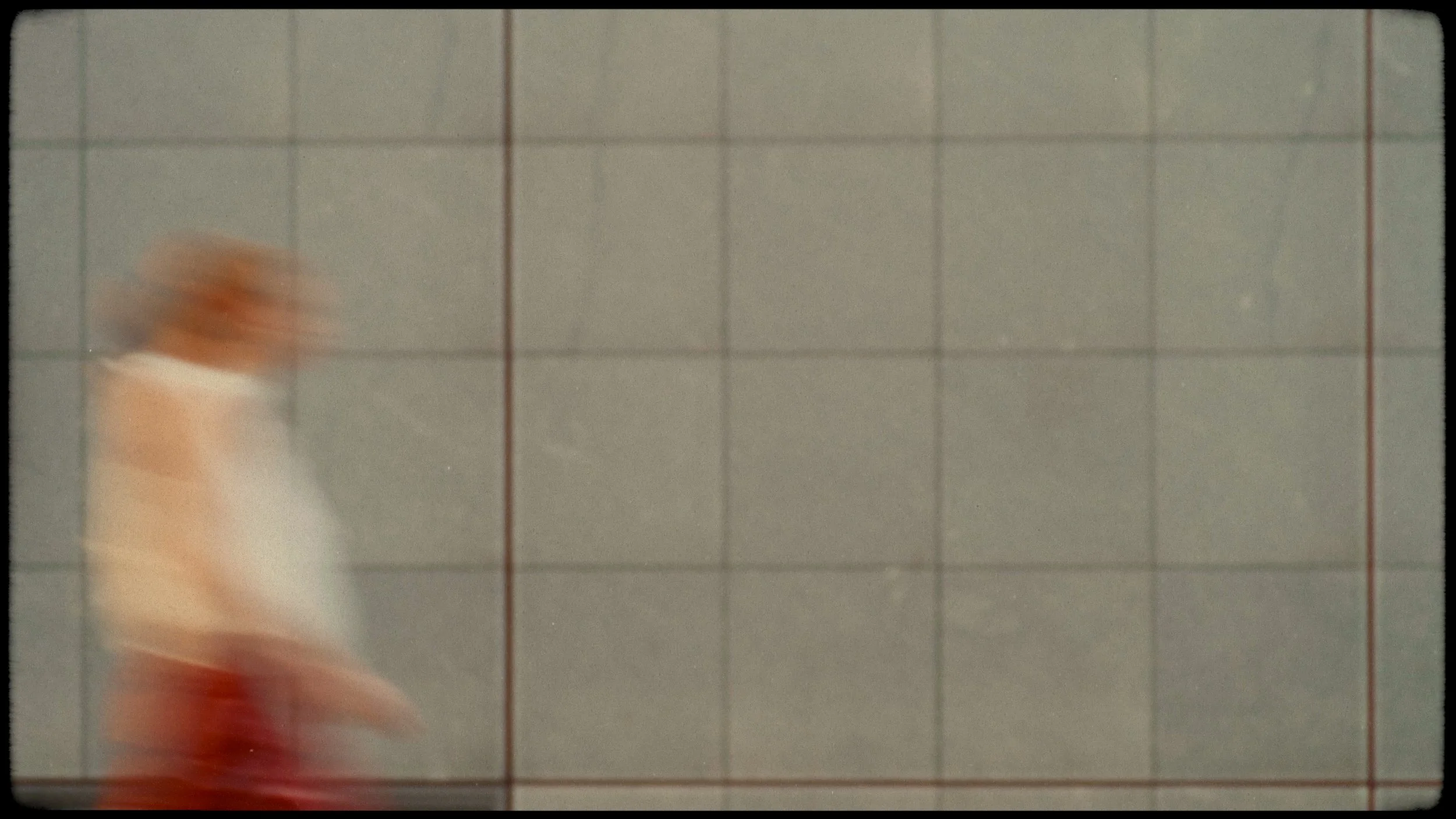 A blurred figure of a woman walking on a tiled sidewalk, with grid lines visible on the ground.