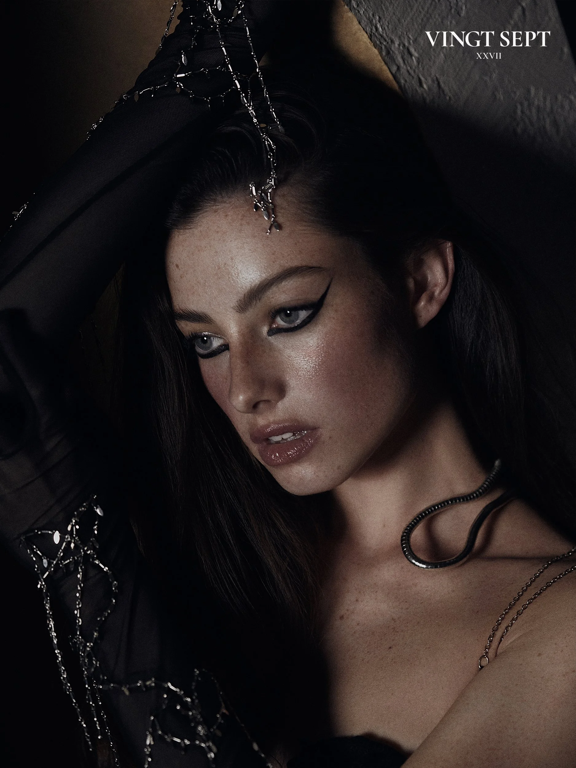 Close-up portrait of a woman with dark hair, bold black eyeliner, glossy lips, and wearing silver jewelry against a dark background, with text "VINTG SEPT" and Roman numeral "XXVII" in the top right corner.